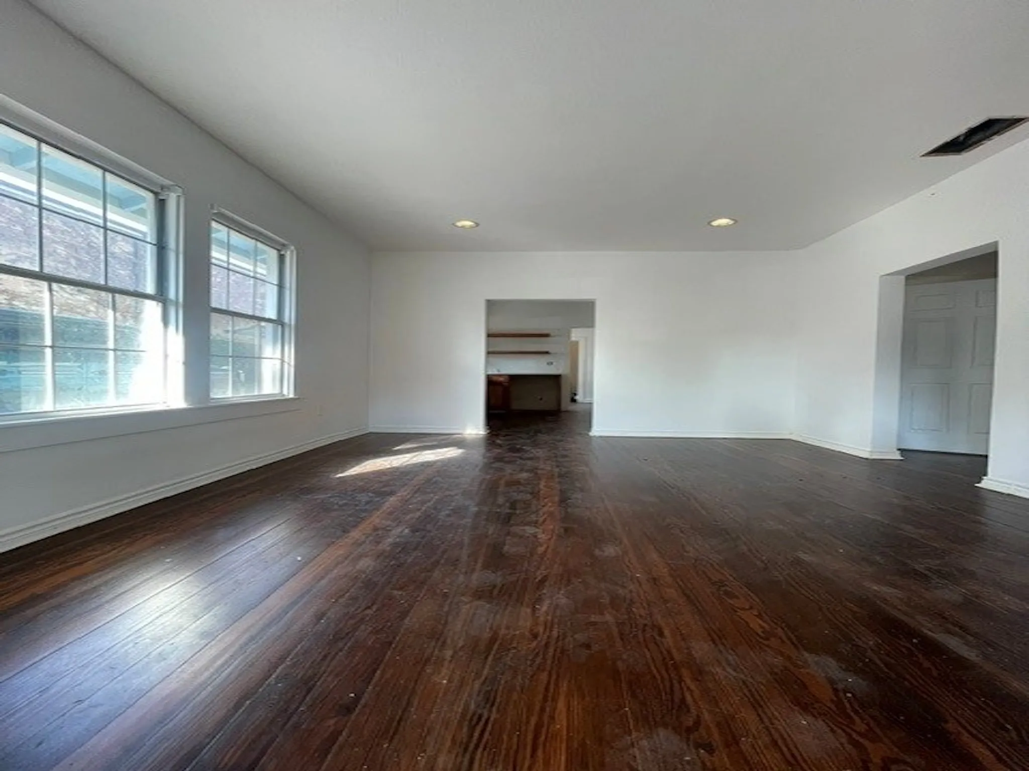 Expansive room featuring rich wood-finish flooring, multiple windows, recessed lighting, and a neutral color palette