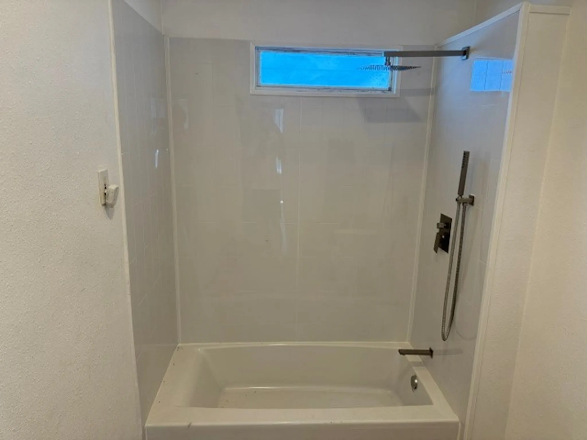 Bathtub with white surround, rainfall showerhead, handheld shower, and horizontal window