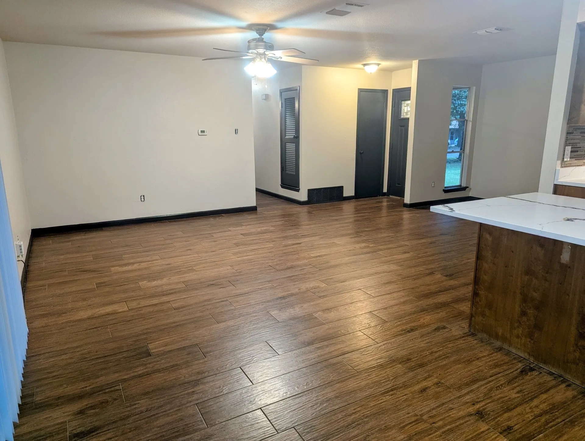 Wood-finish flooring throughout, ceiling fan with integrated lighting, and a kitchen island featuring a light-toned countertop