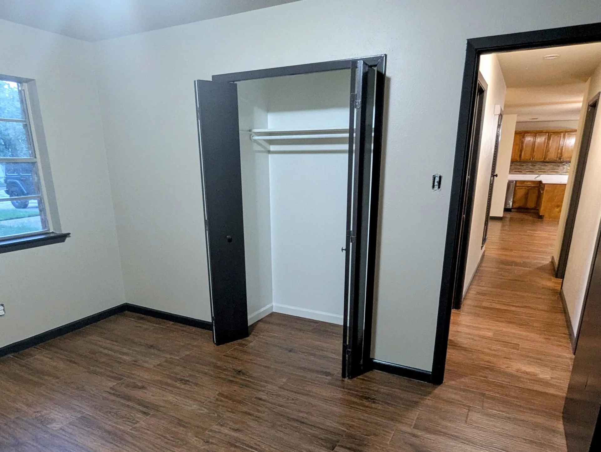 Wood-finish flooring, white walls, black trim, and a built-in closet with bifold doors