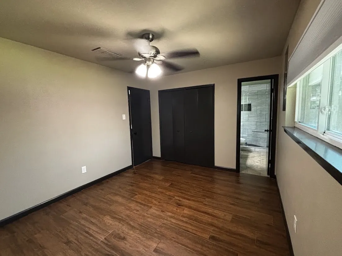 Wood-finish flooring with dark baseboards, a ceiling fan with integrated lighting, and a window with blinds