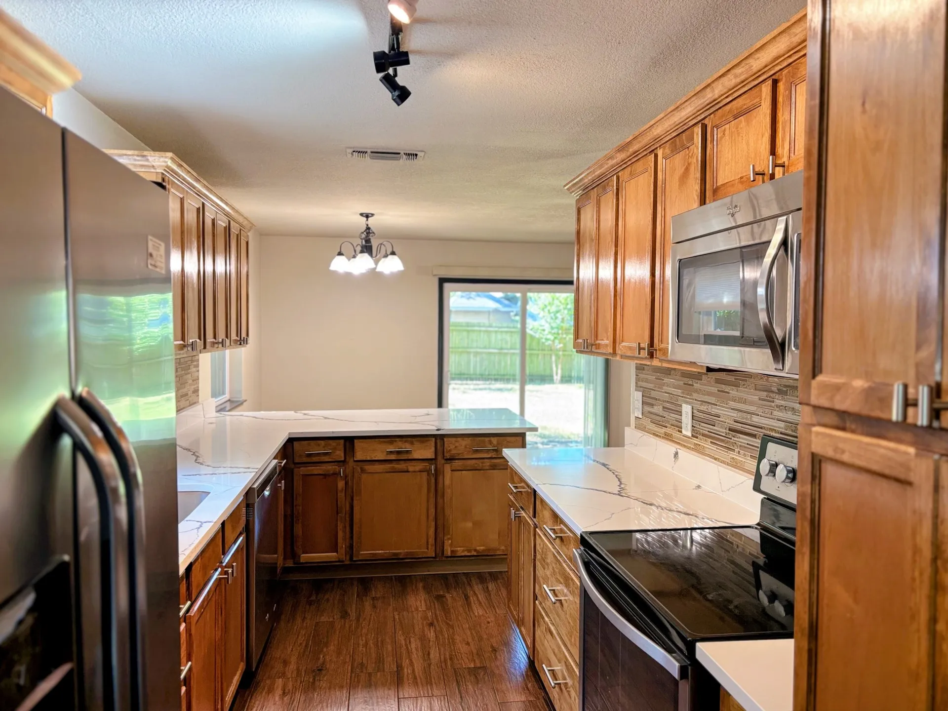 Wood-finish flooring, wood cabinetry, stone countertops, stainless steel appliances, and a tile backsplash