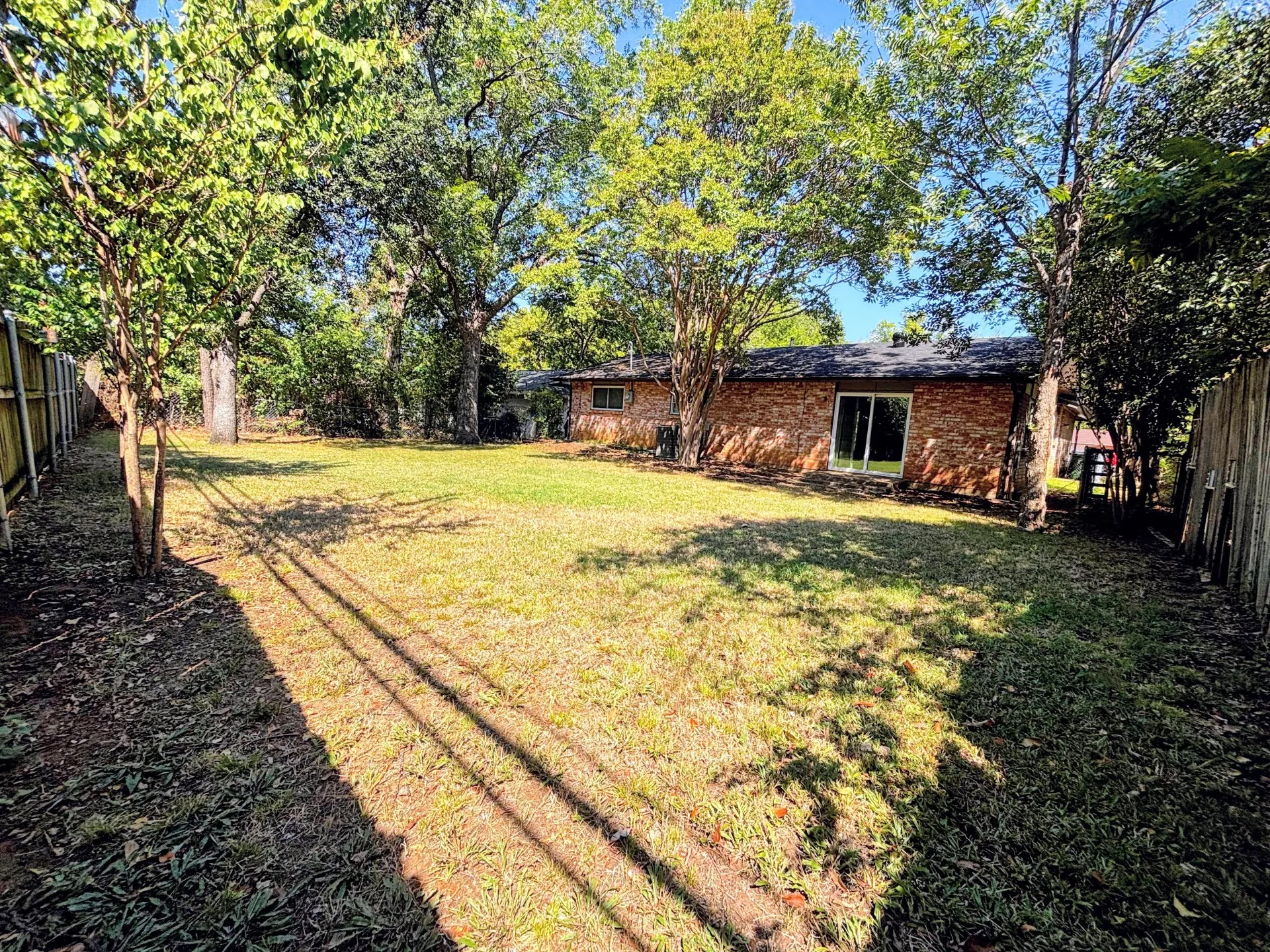 Expansive backyard with a brick exterior, mature trees, wood fencing, and sliding glass doors