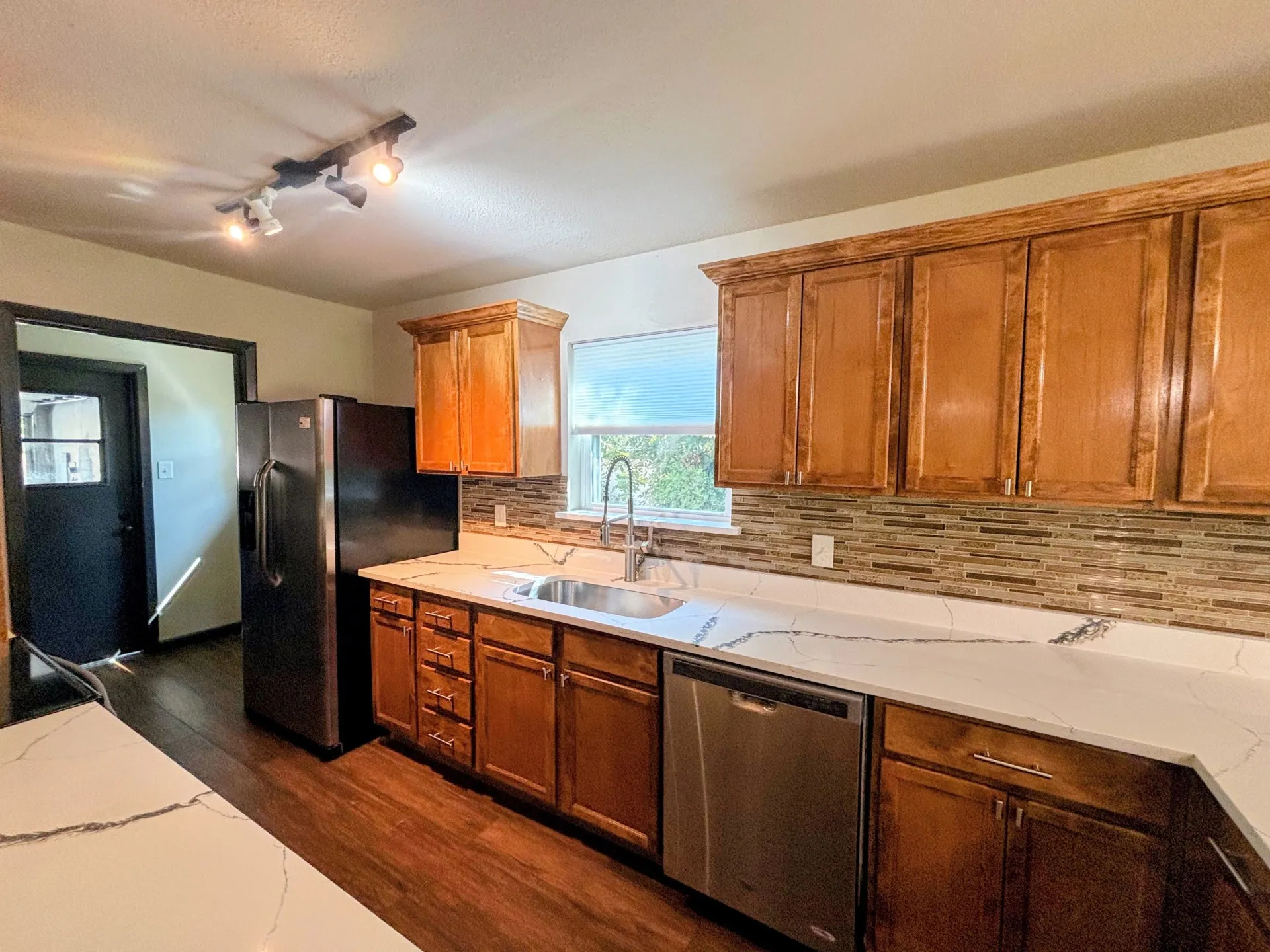 Wood-finish flooring with track lighting, wood cabinetry, and stainless steel appliances