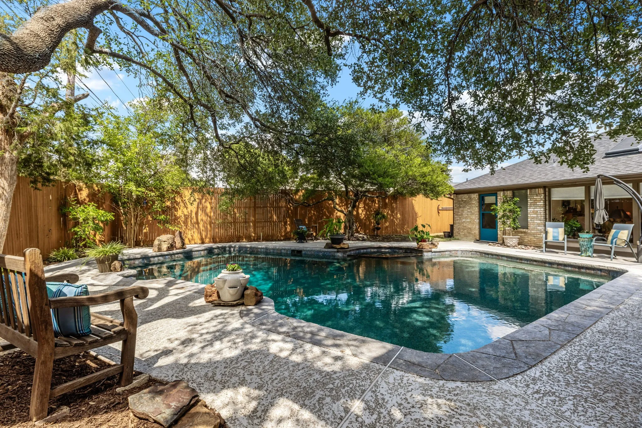 Private backyard oasis featuring a swimming pool with stone coping, a spacious patio area, mature trees, and a privacy fence