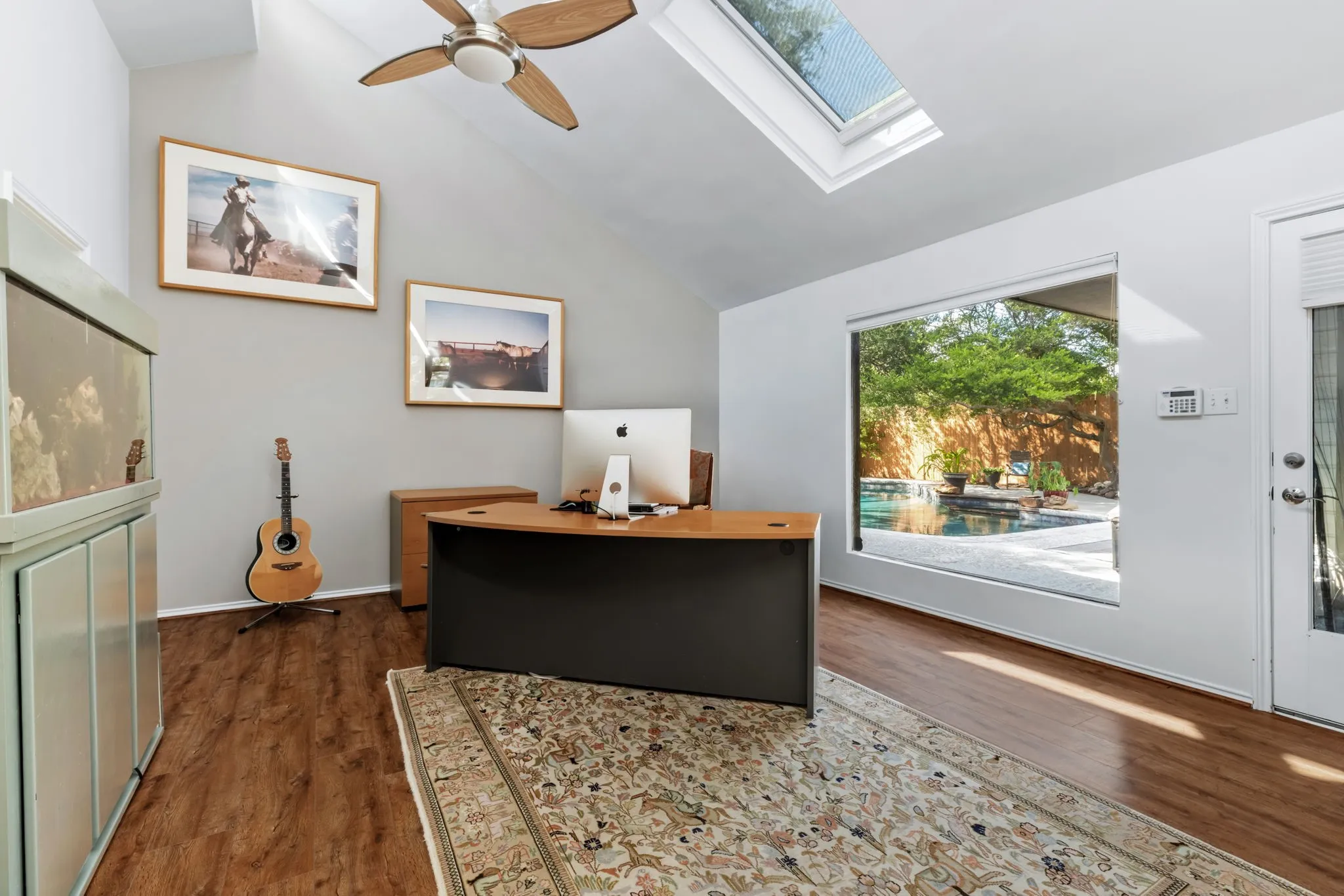 Bright, open office space featuring soaring vaulted ceilings with skylights, warm wood-finish flooring, and a large picture window framing outdoor scenery