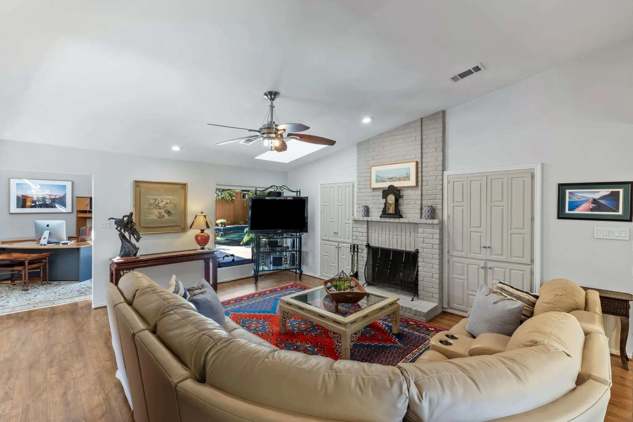 Vaulted ceiling, wood-finish flooring, brick fireplace with mantel, built-in cabinetry, and ceiling fan with integrated lighting