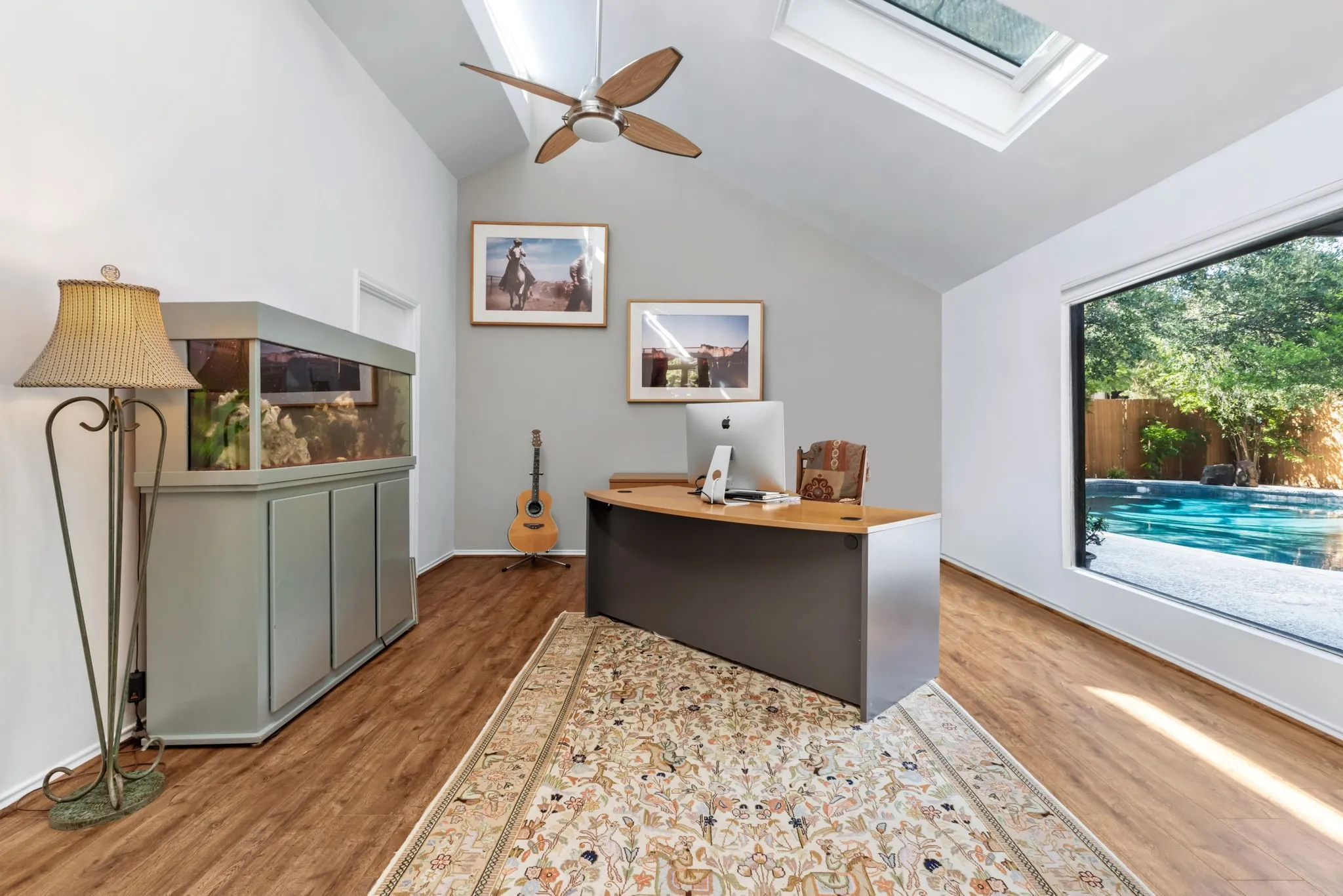 Vaulted ceiling with skylight, wood-finish flooring, ceiling fan, and large picture window overlooking a swimming pool