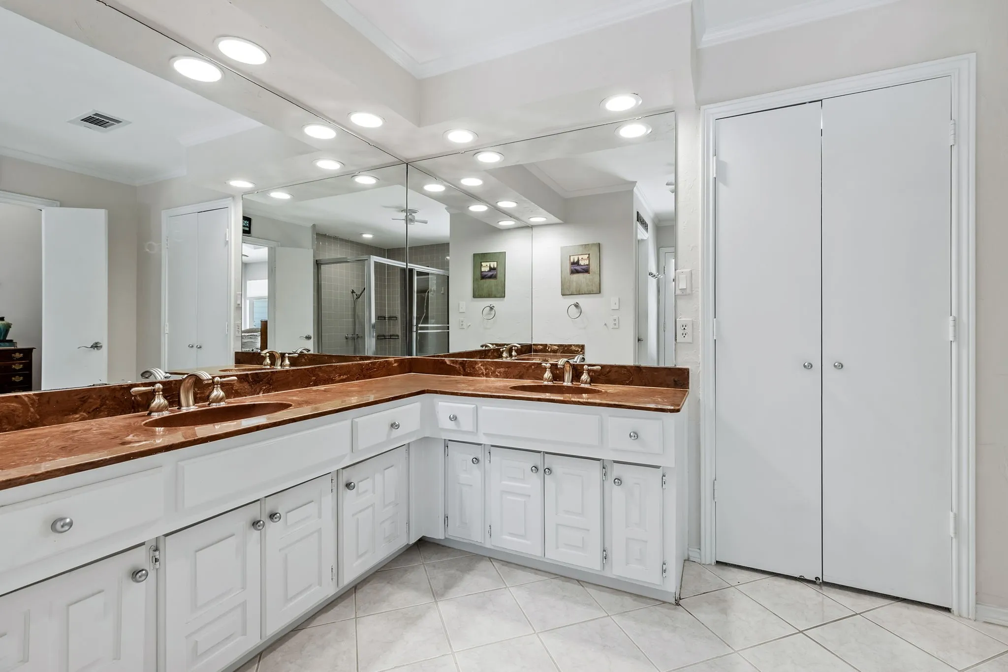 Double vanity with integrated sinks, expansive counter space, white cabinetry, and a full-width mirror with recessed lighting