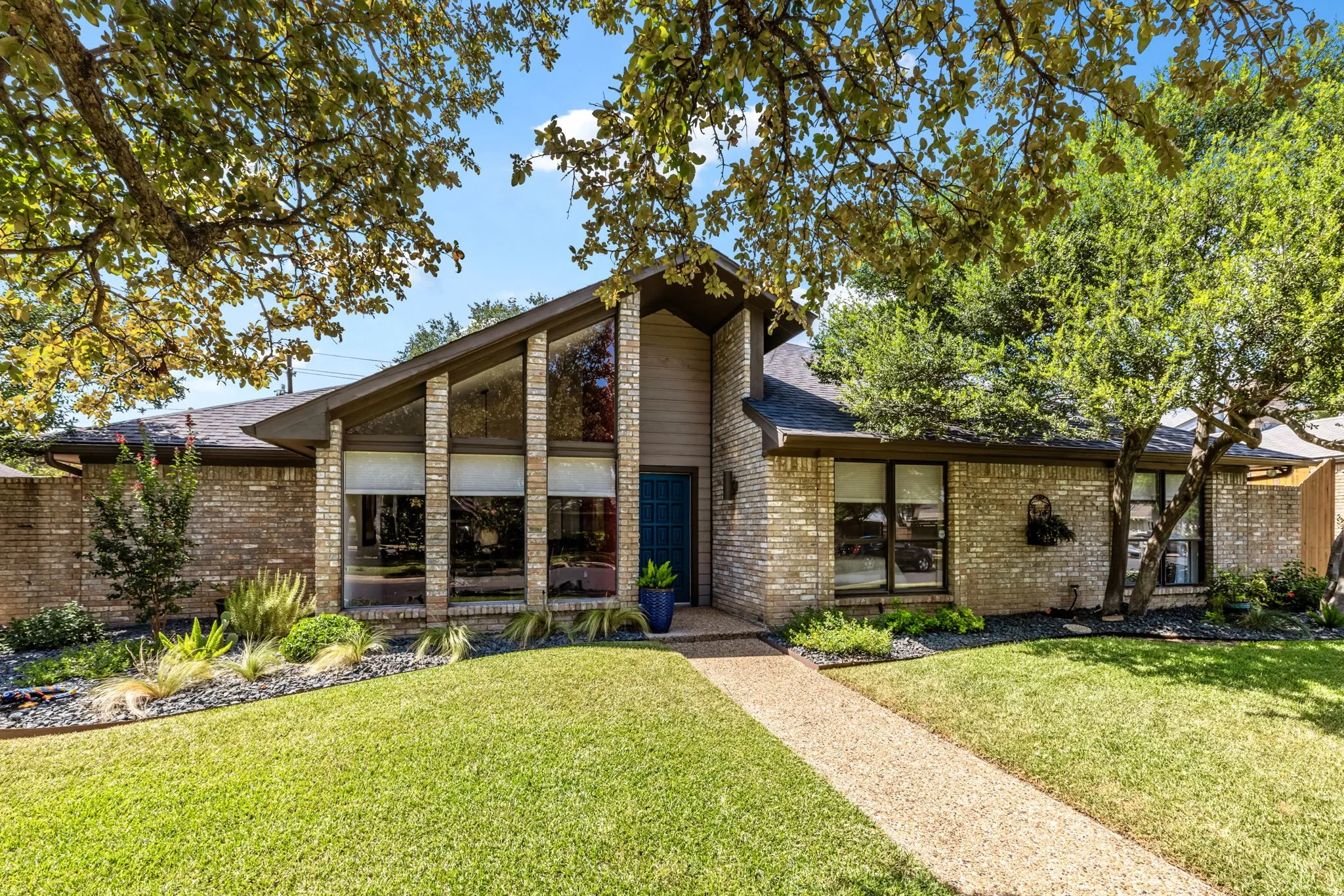 Brick exterior with a prominent A-frame architectural feature, expansive front windows, and mature trees providing shade