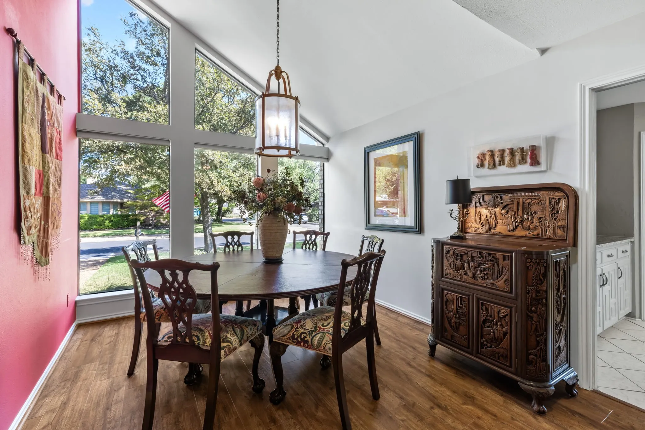 Vaulted ceiling with a hanging lantern fixture, large pane windows, wood-finish flooring, and a brightly painted accent wall