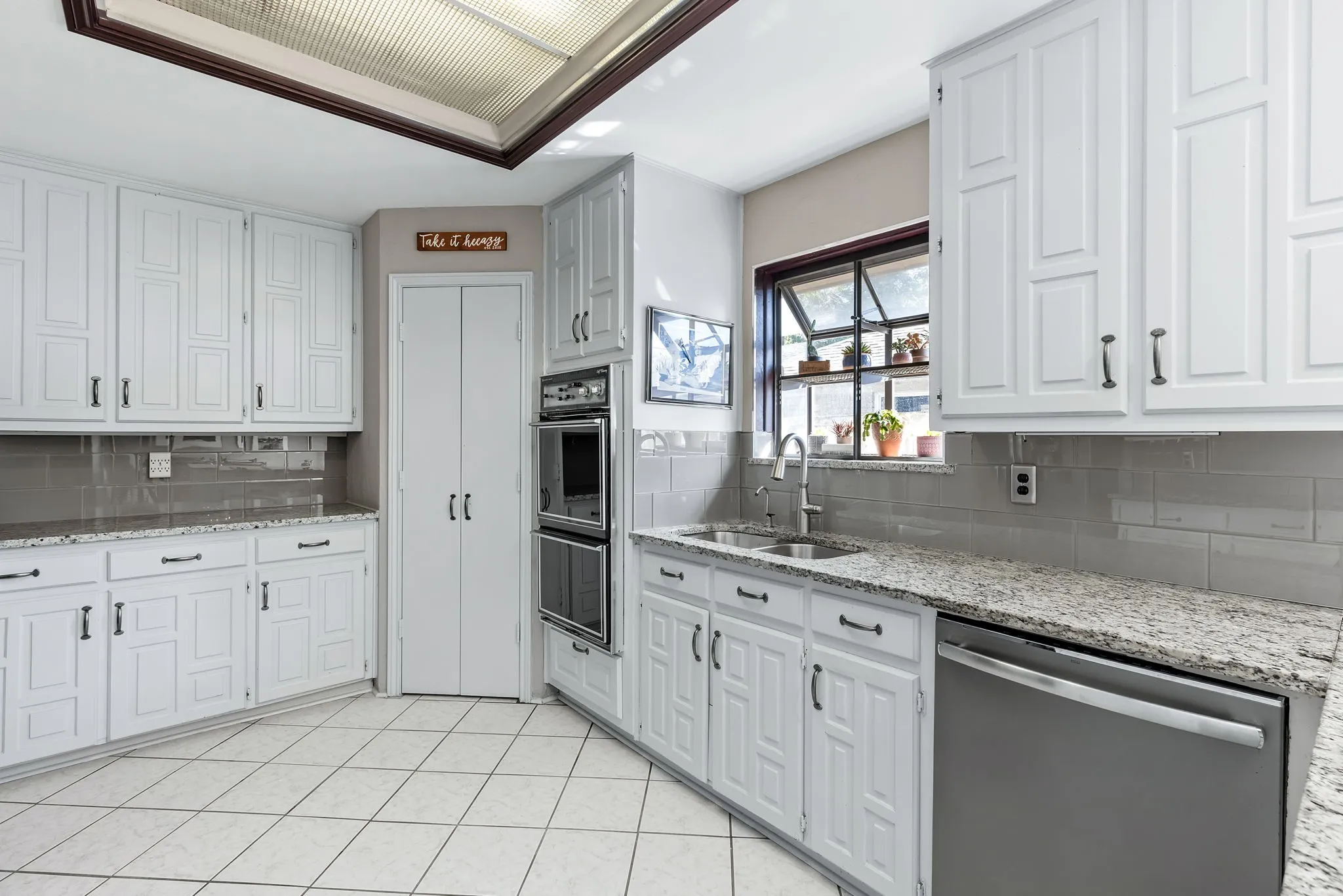 White cabinetry with dark hardware, stone countertops, stainless steel appliances, tile flooring, and a subway tile backsplash