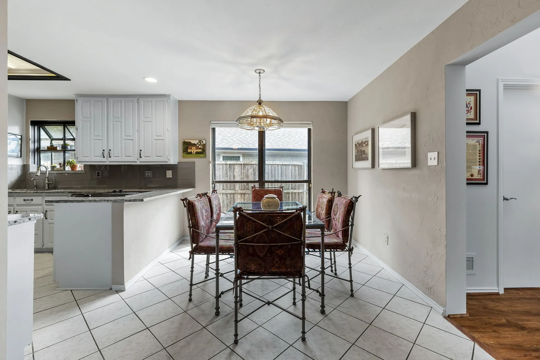 White cabinetry, tile flooring, built-in breakfast bar, pendant lighting, and a large window