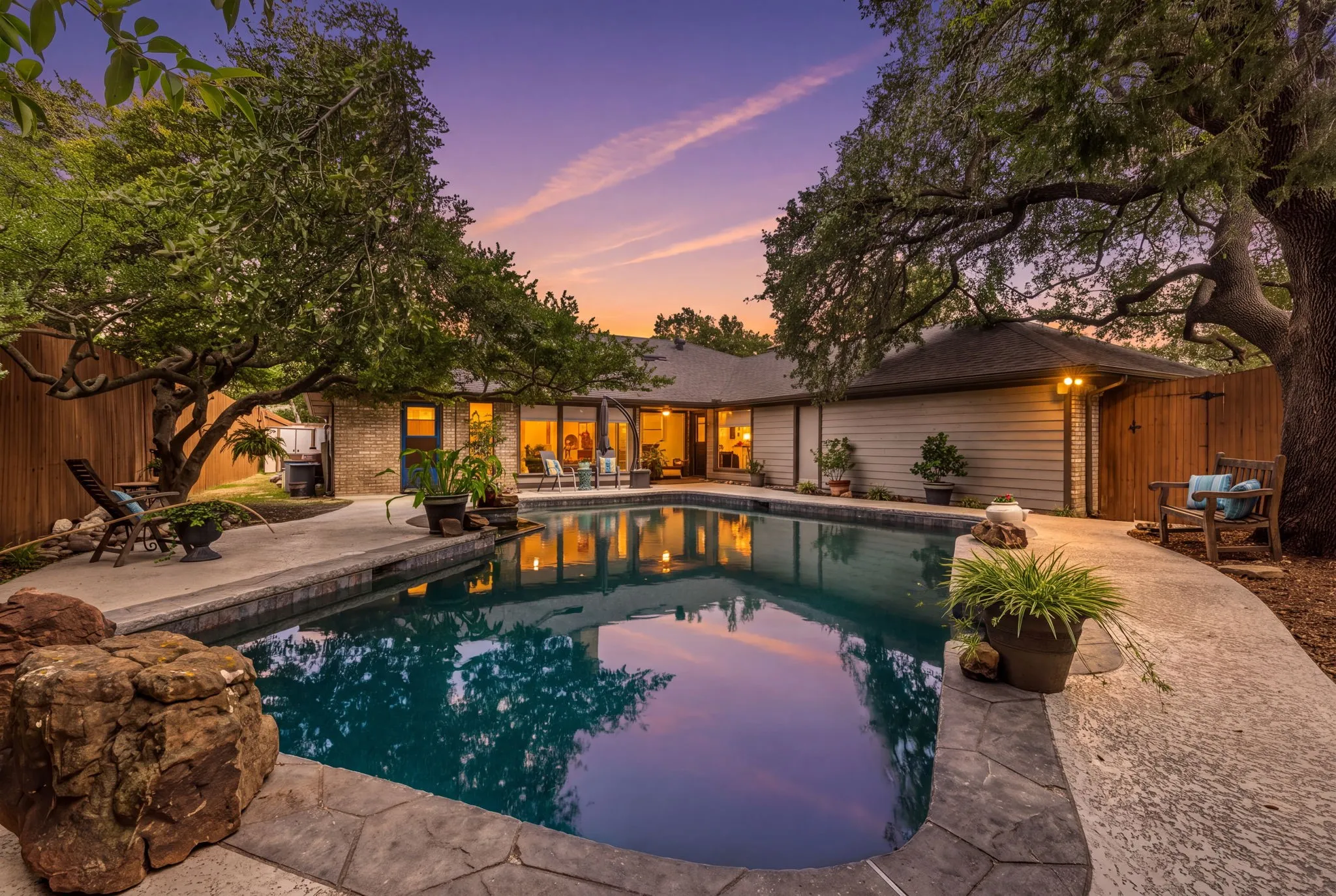 Swimming pool with stamped concrete decking, surrounded by mature trees and a private wooden fence