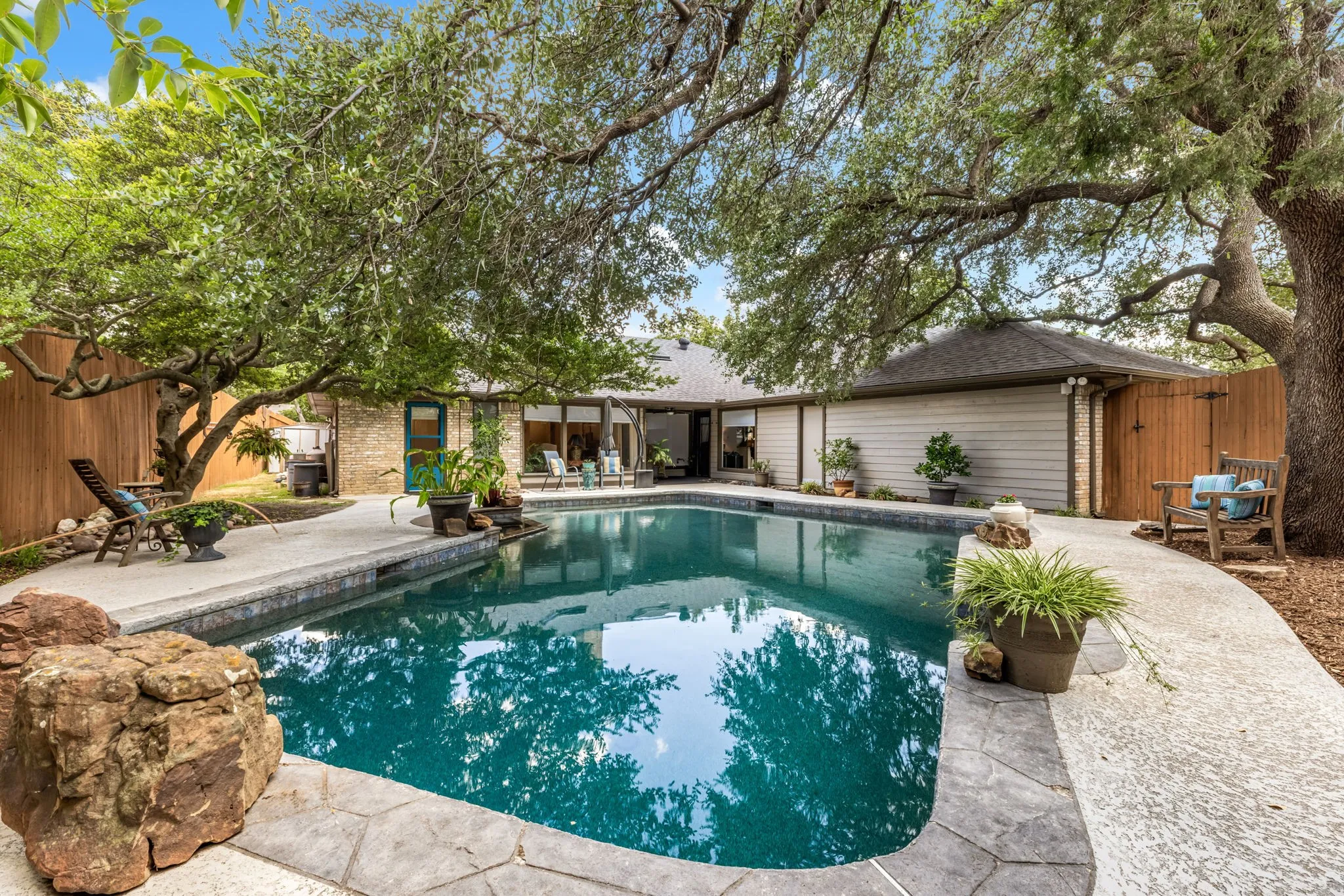 Swimming pool with flagstone coping, surrounding concrete patio, and mature trees providing shade