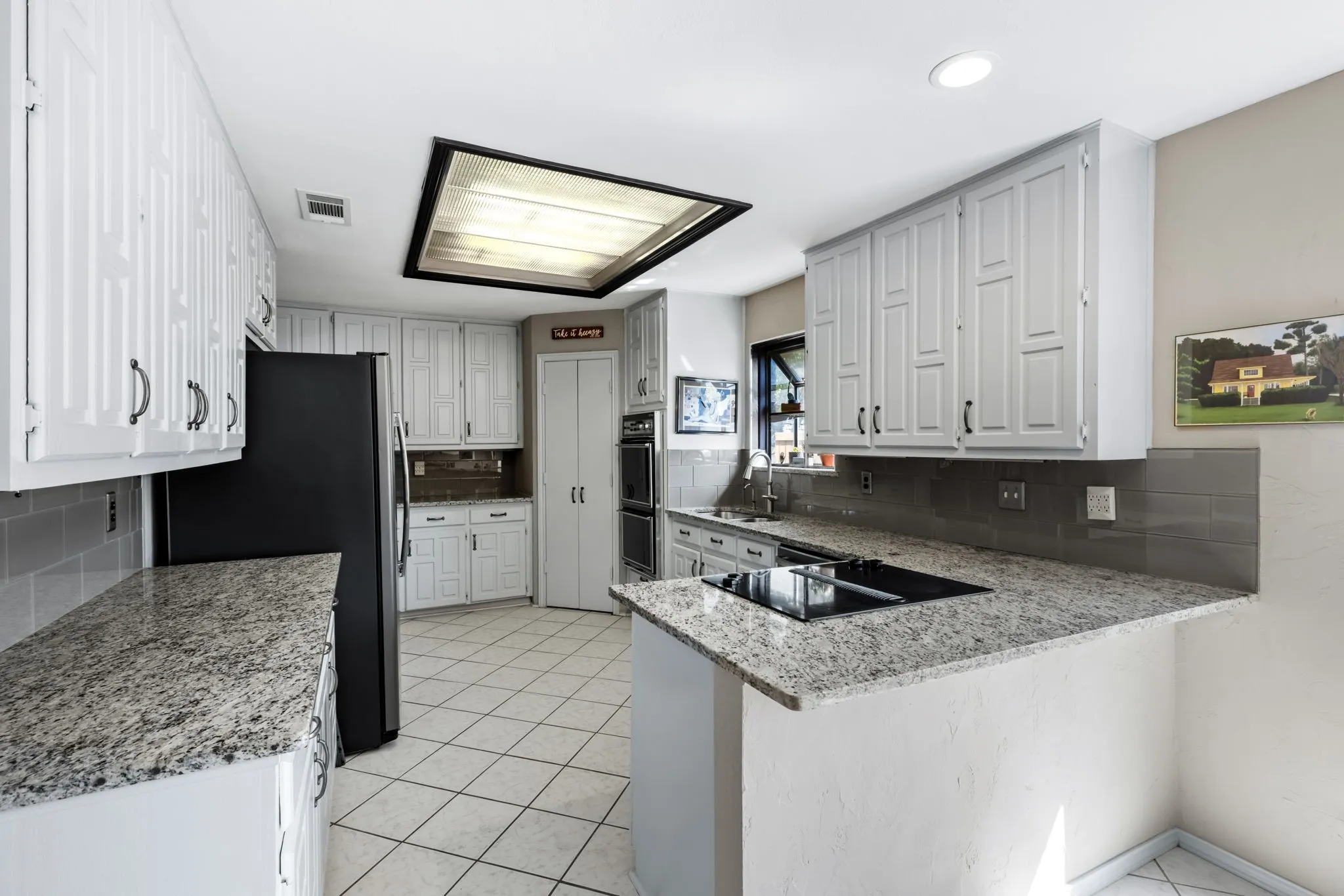 Kitchen featuring white cabinetry, light granite countertops, tile flooring, and integrated cooktop