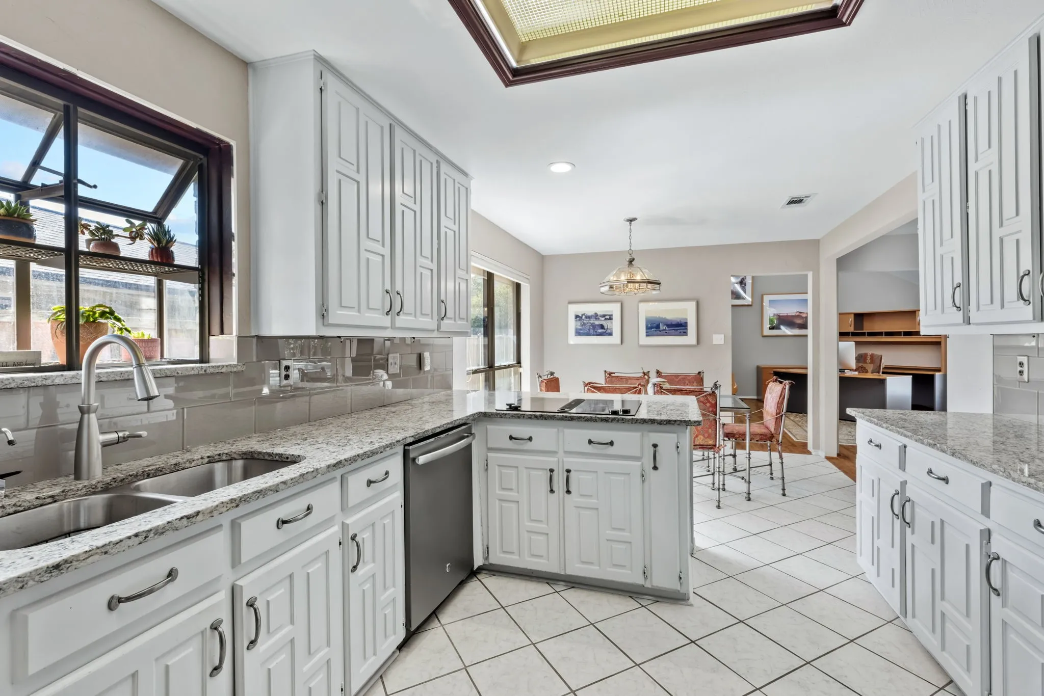 Kitchen featuring white cabinetry, light-toned countertops, a stainless steel sink, tile flooring, and a skylight