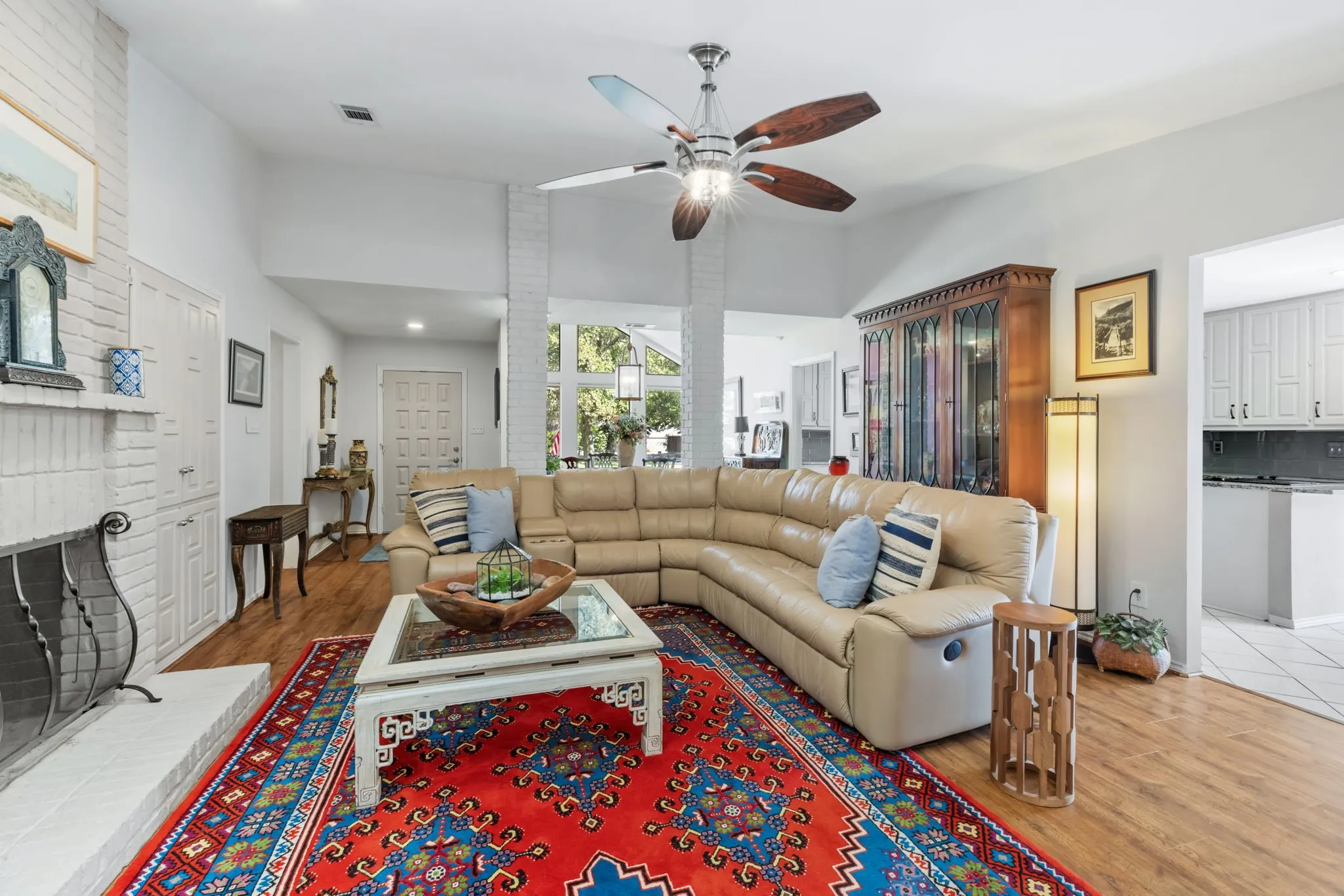 Vaulted ceilings, wood-finish flooring, white painted brick fireplace with hearth, and a contemporary ceiling fan