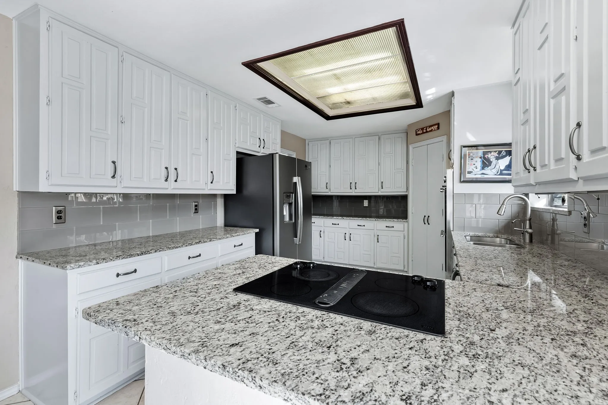 Kitchen featuring white cabinetry, light-toned countertops, a built-in electric cooktop, and a stainless steel refrigerator