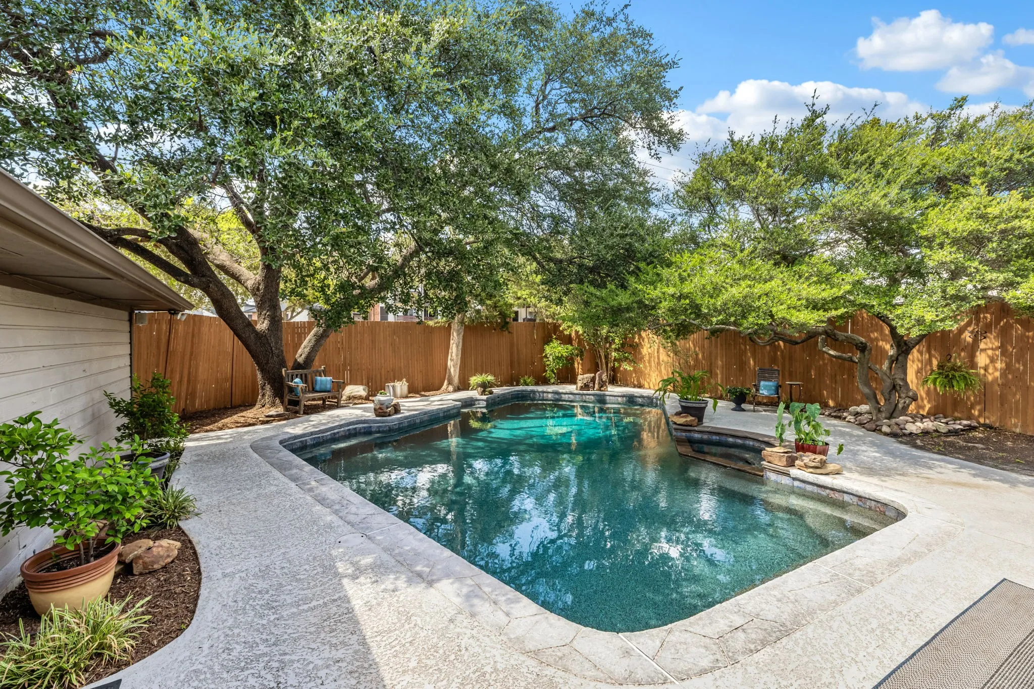 Swimming pool with stone coping and integrated steps, surrounded by a textured concrete patio