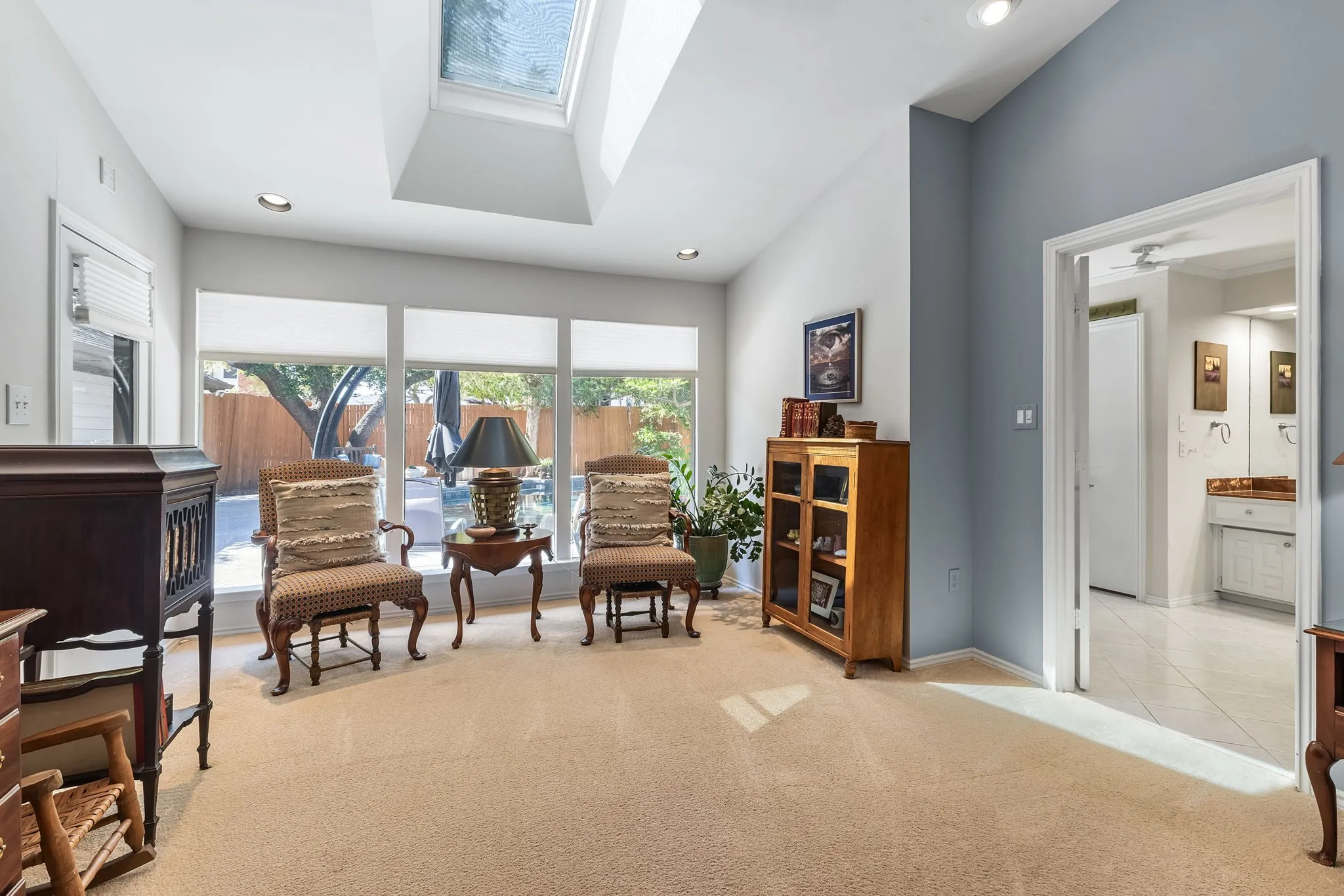 Vaulted ceiling with skylight, recessed lighting, expansive window wall, light-toned carpeting, and a doorway opening to a tiled space