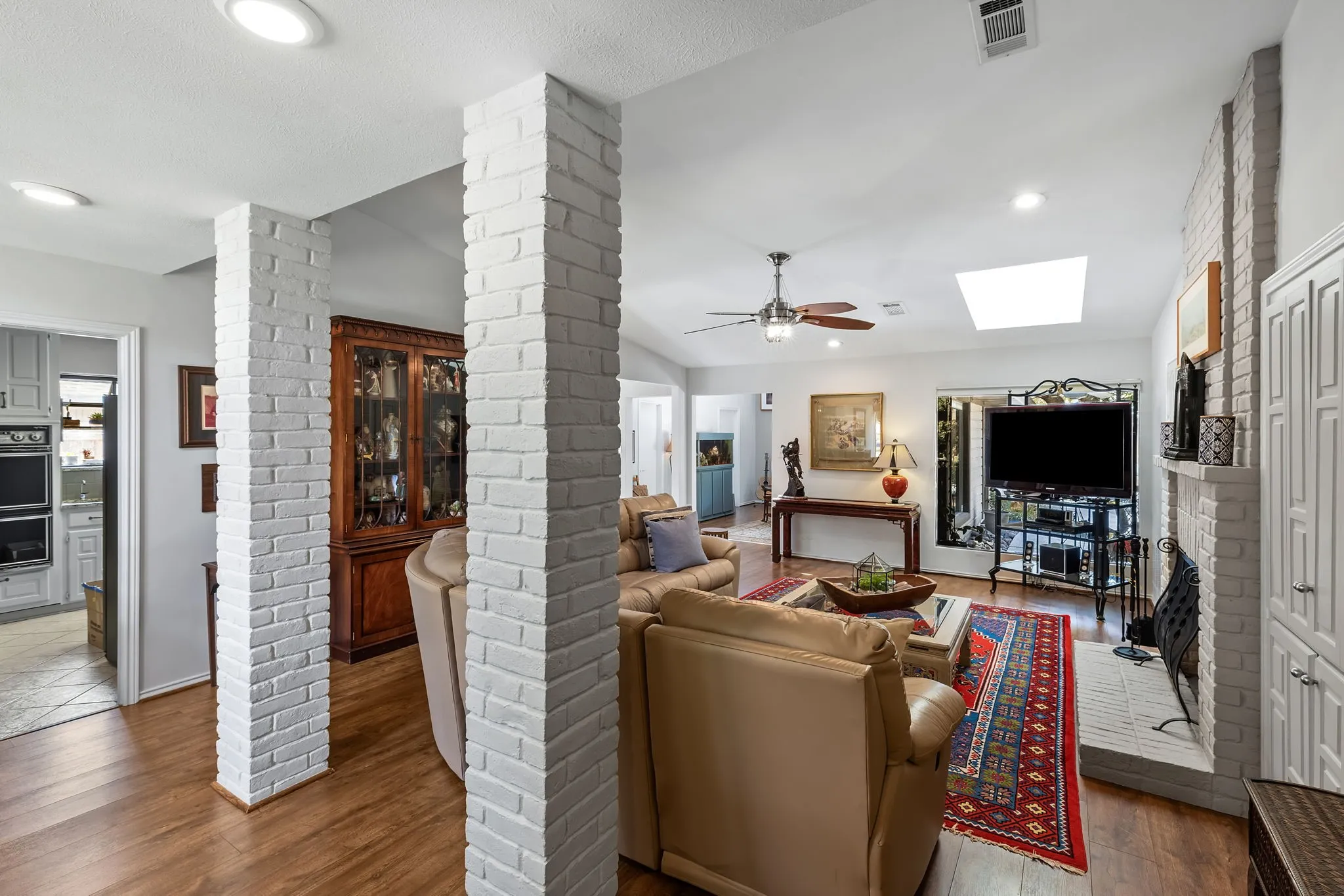 Vaulted ceiling living area featuring a skylight, wood-finish flooring, white-painted brick columns, and a brick fireplace with built-in cabinetry