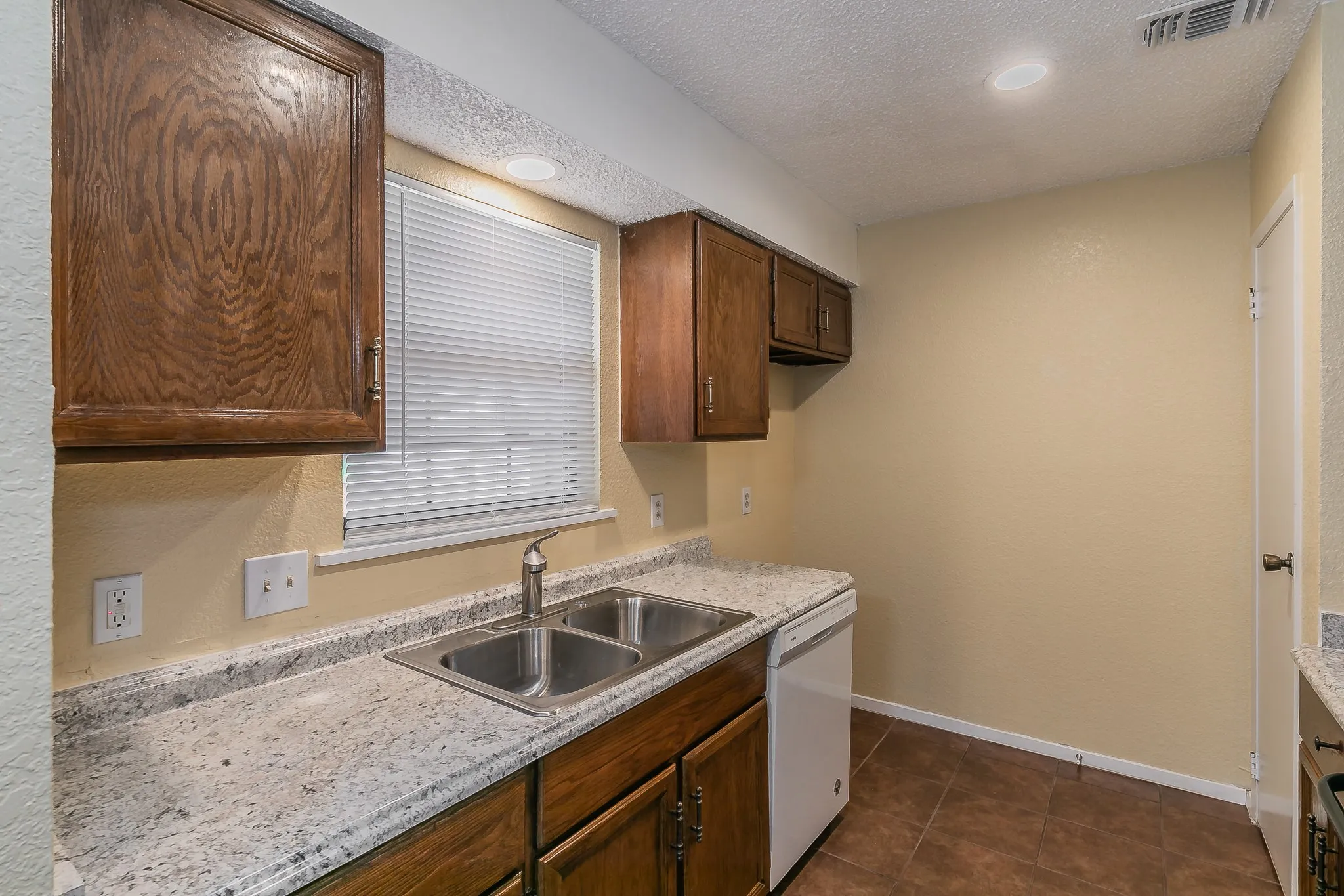 Kitchen featuring dark tile patterned floors, white dishwasher, sink, and a textured ceiling