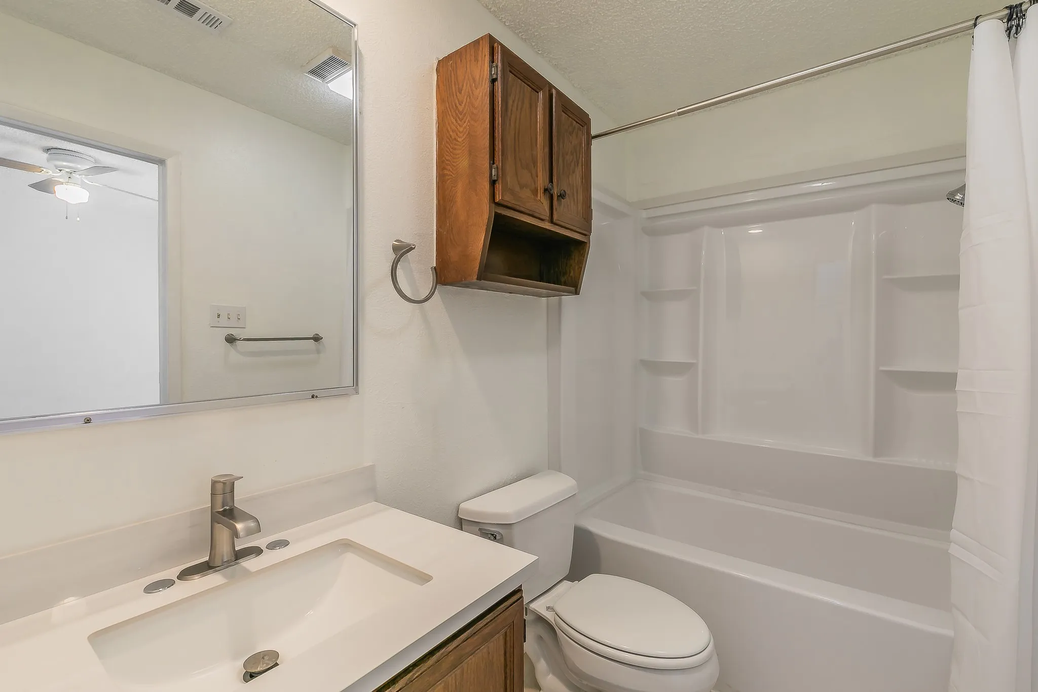 Full bathroom featuring a textured ceiling, toilet, vanity, ceiling fan, and shower / tub combo