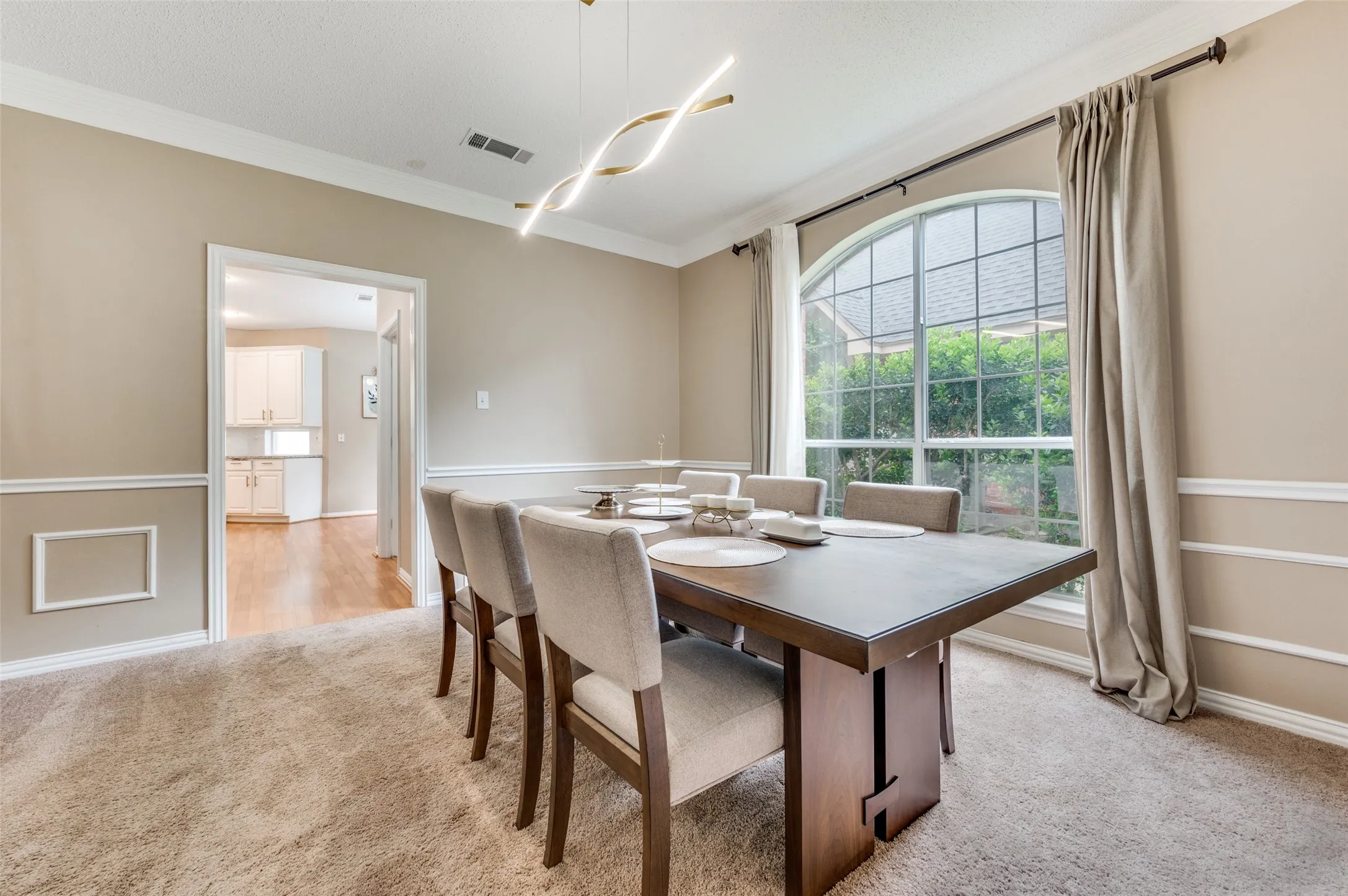 Arched window with gridded panes, crown molding, chair rail molding, wall paneling, and a contemporary linear light fixture
