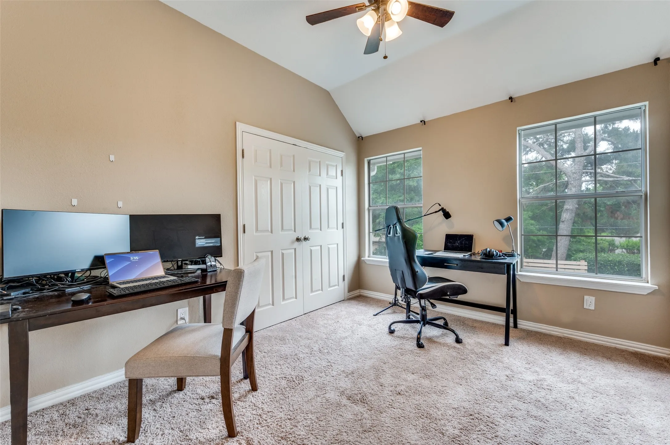 Vaulted ceiling with a ceiling fan, dual windows, and light beige carpeting