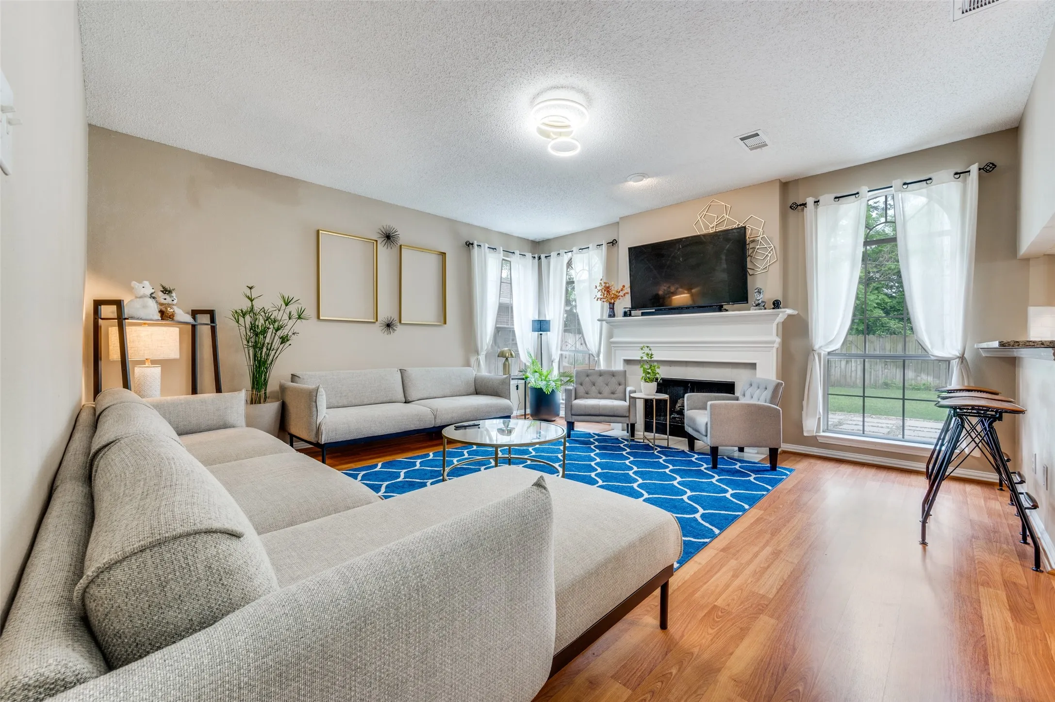 Bright, open living room featuring hardwood flooring, a gas fireplace with surround mantel, recessed ceiling lighting, and expansive windows with natural light