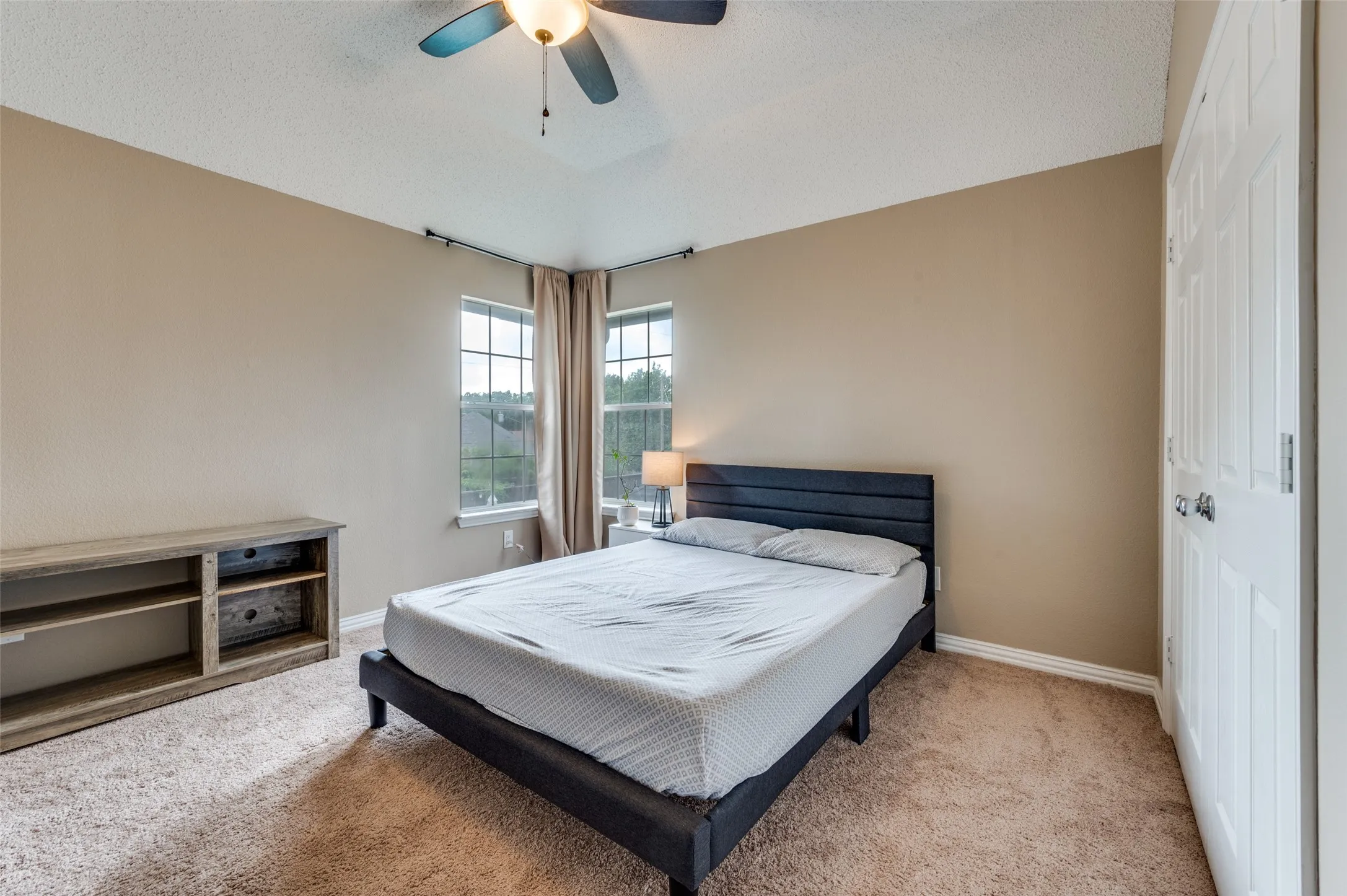 Vaulted ceiling with a ceiling fan, carpeted flooring, two windows with blinds, and an interior door