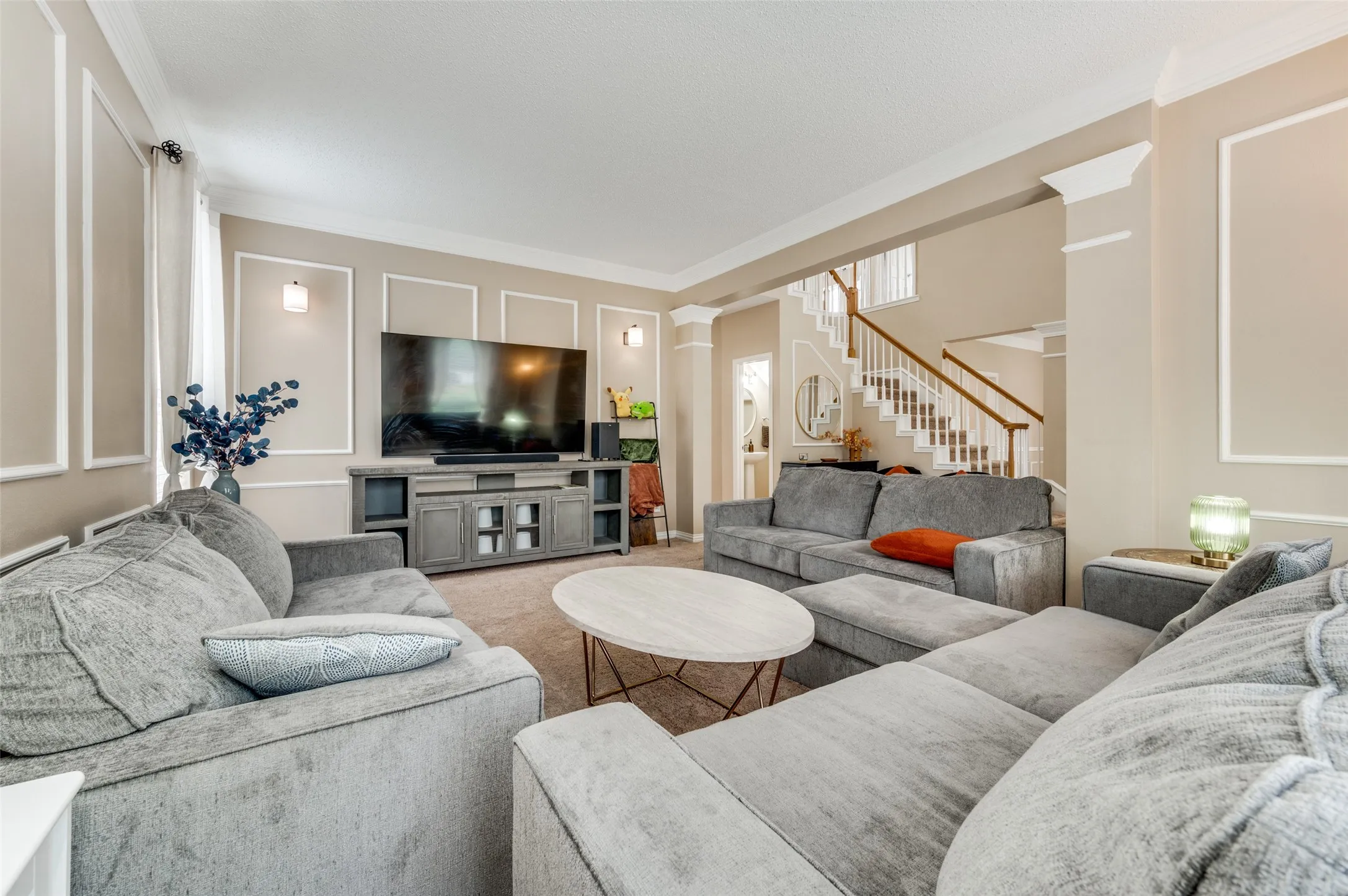 Living area featuring crown molding, wall paneling, sconce lighting, and a prominent staircase with wood newel posts and railings