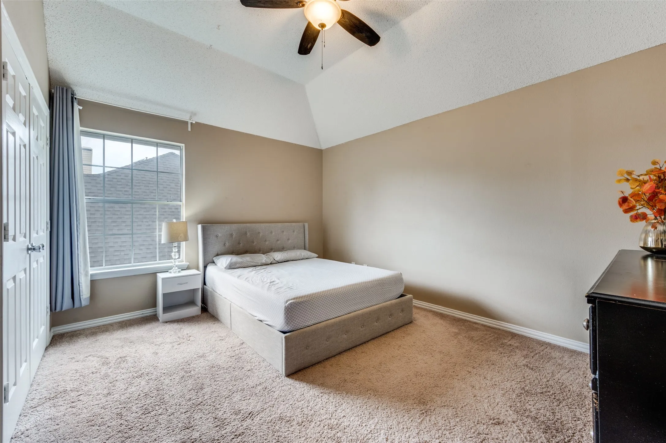 Vaulted ceiling with a ceiling fan, carpet flooring, and a large window