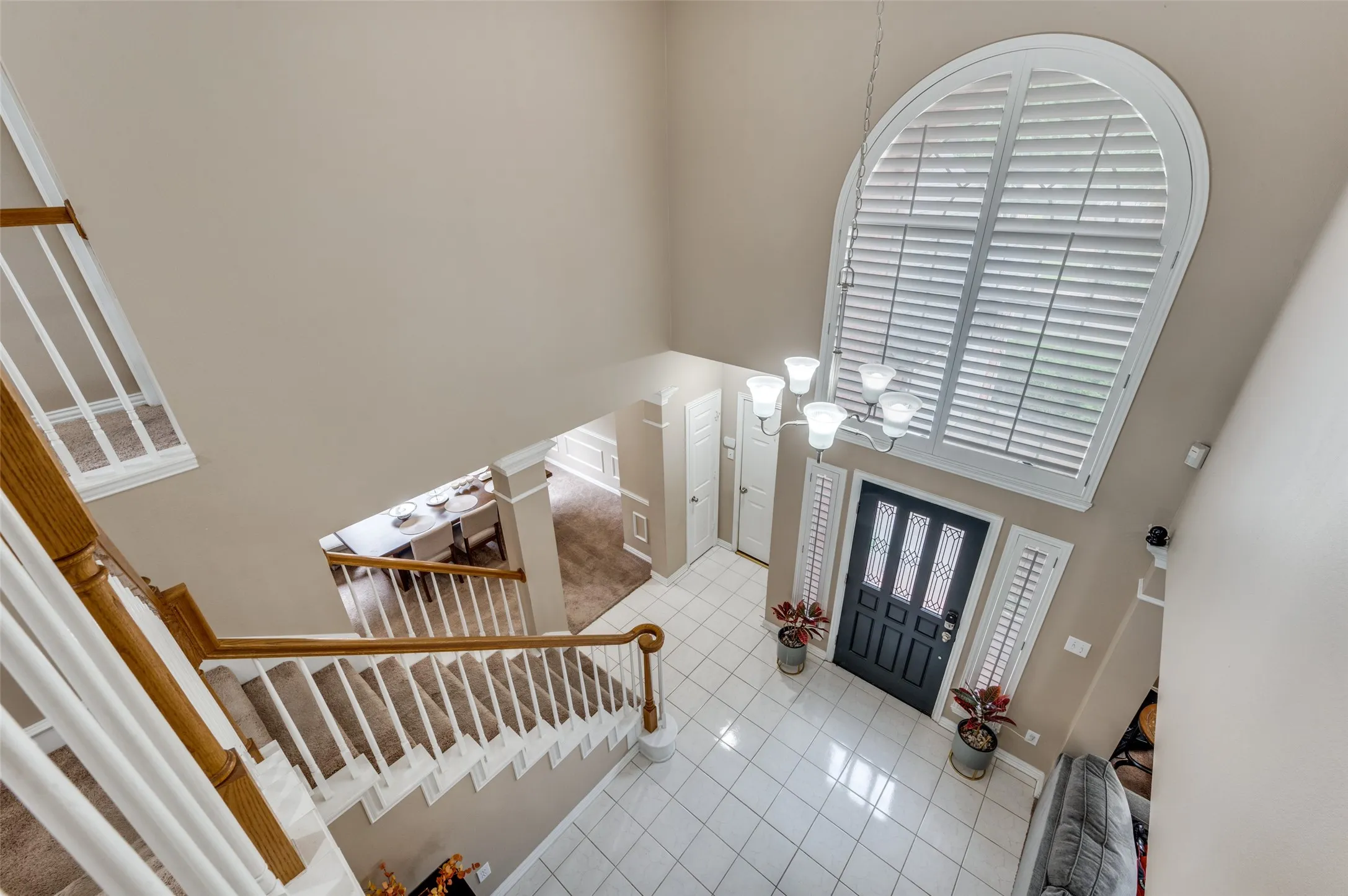 Two-story foyer featuring a grand arched window with plantation shutters, tile flooring, and a chandelier