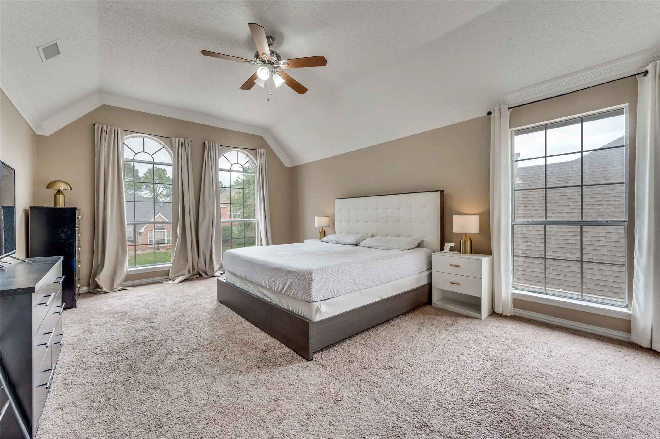 Vaulted ceiling with a ceiling fan, plush carpet flooring, and multiple windows including two arched windows
