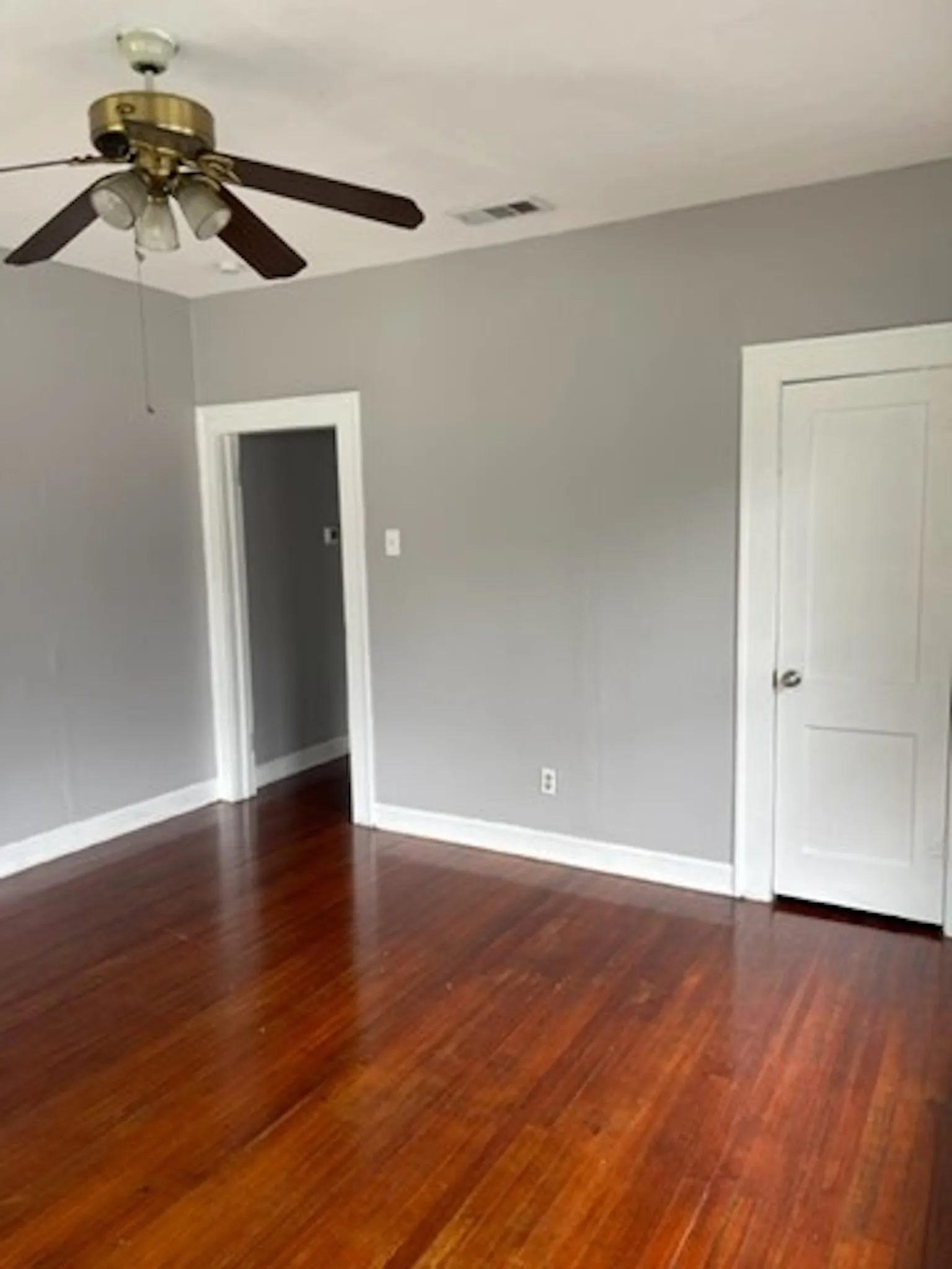 Unfurnished room featuring dark wood-style floors, visible vents, baseboards, and a ceiling fan