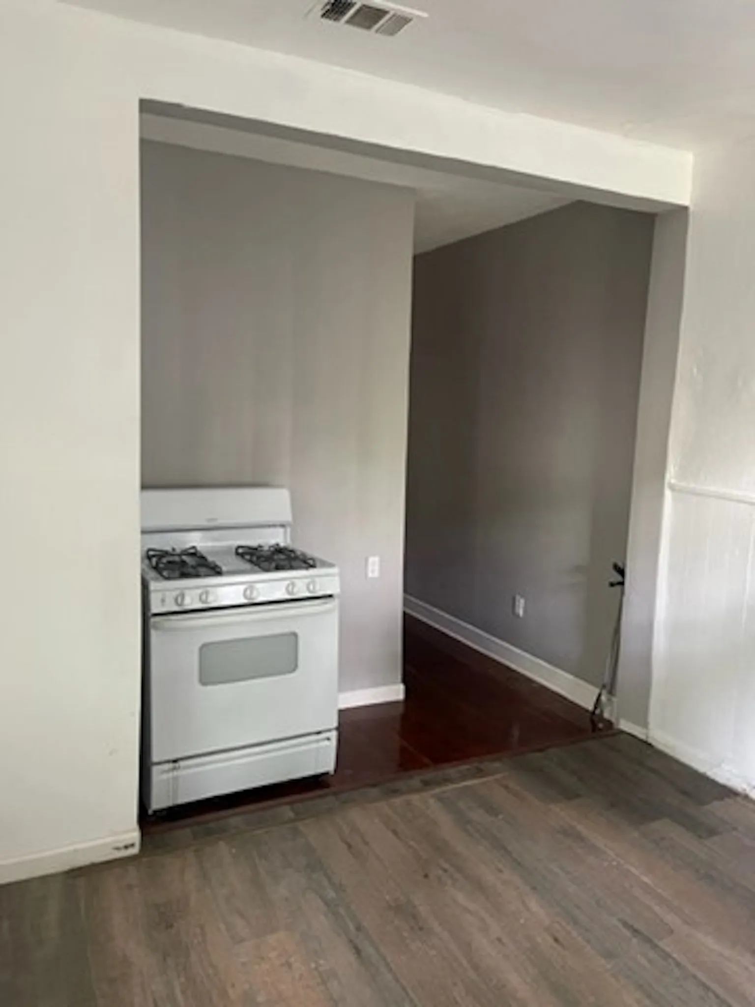 Kitchen featuring dark wood-type flooring, visible vents, white gas stove, and baseboards