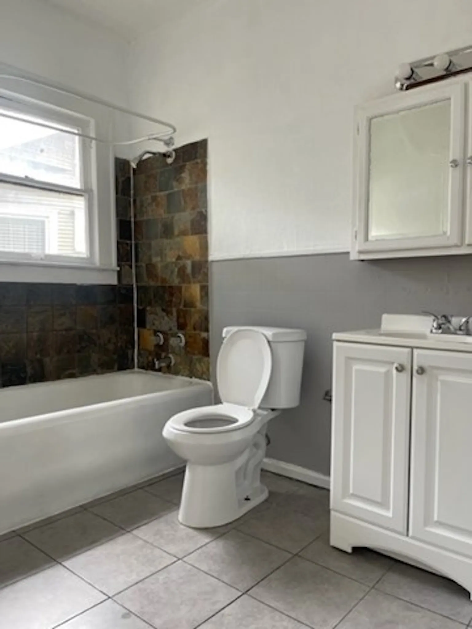 Bathroom with toilet, a wainscoted wall, tile patterned flooring, tub / shower combination, and vanity