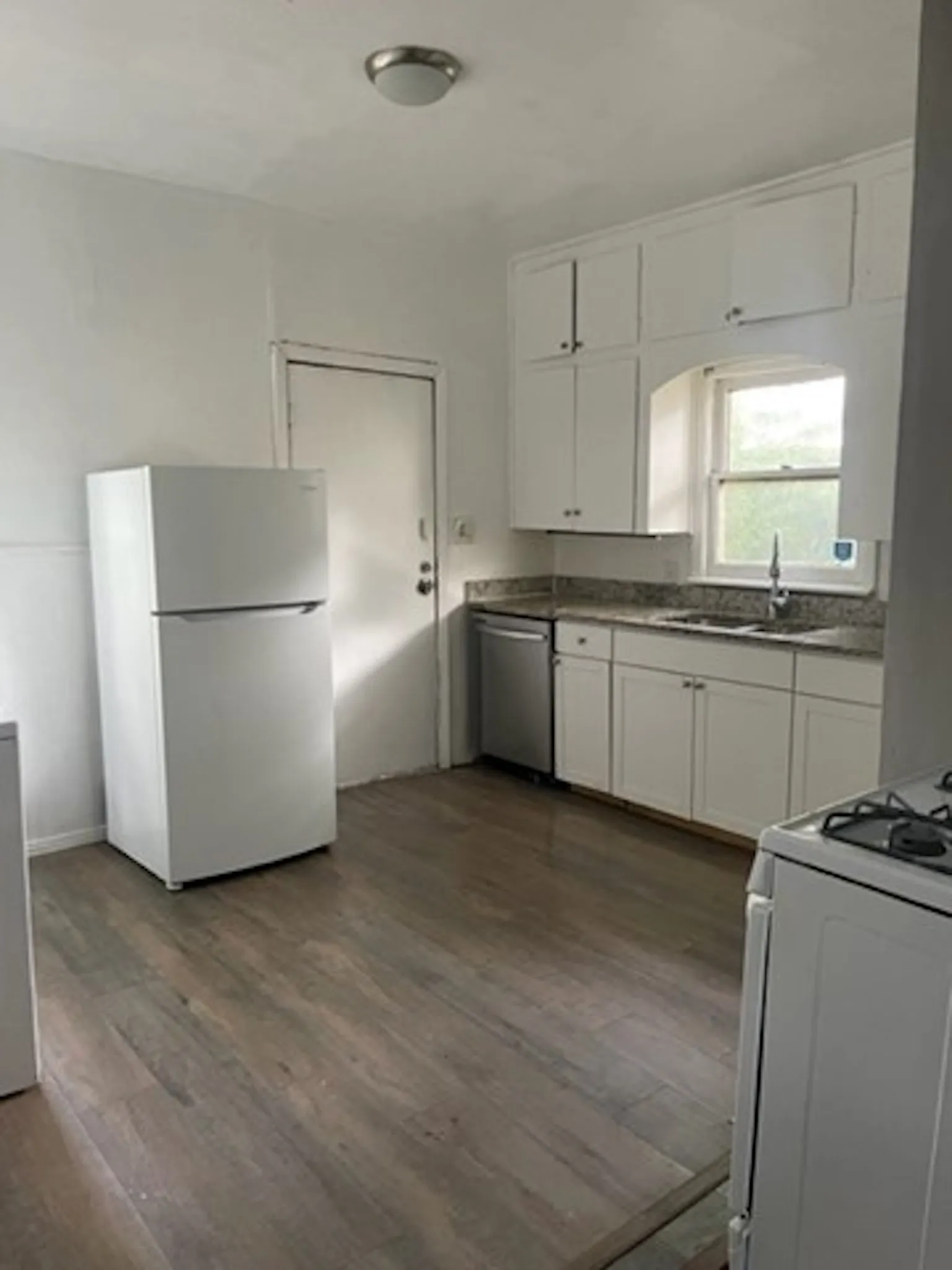 Kitchen featuring white appliances, dark countertops, dark wood-type flooring, white cabinetry, and a sink