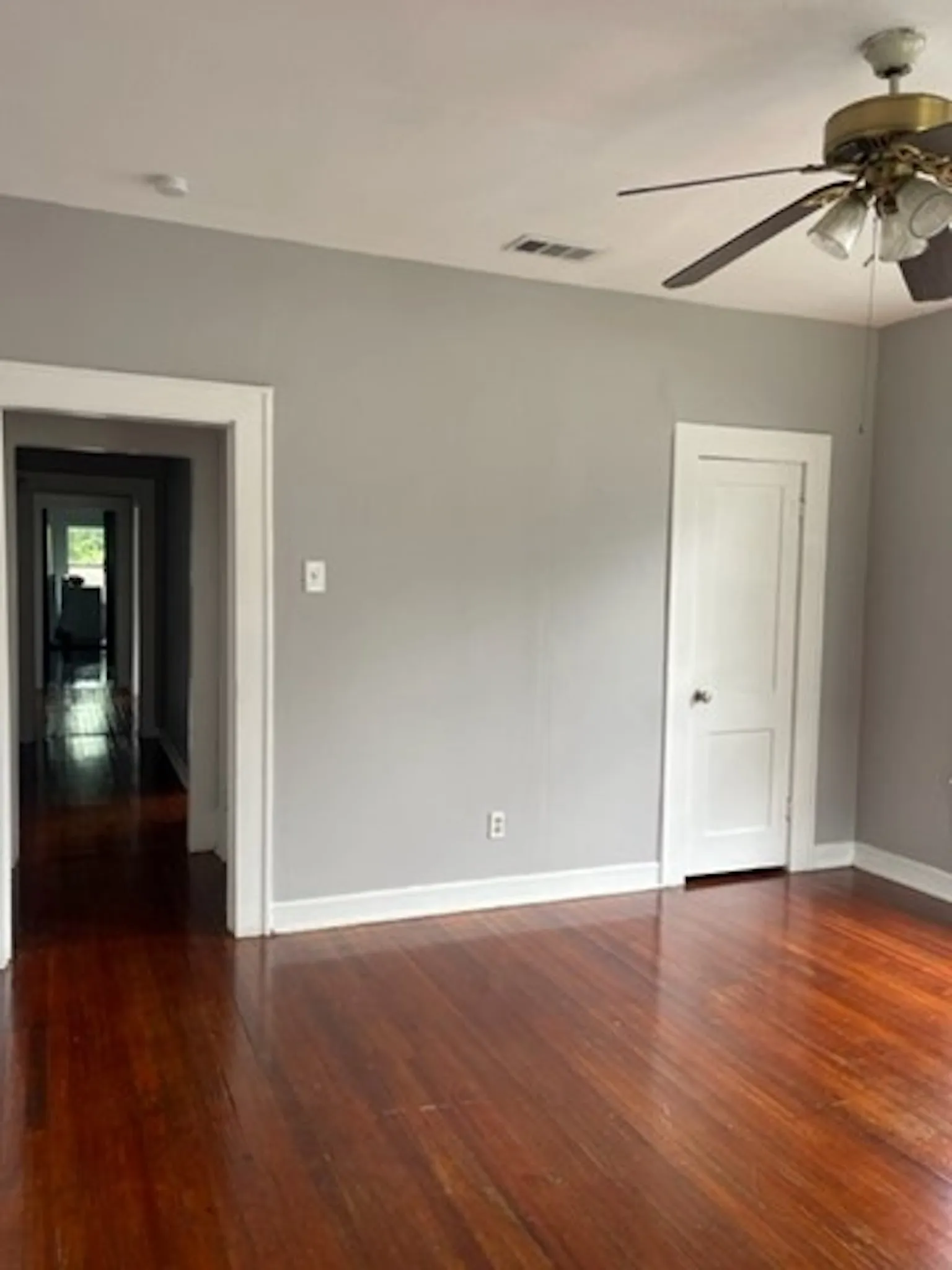 Unfurnished room with dark wood-style floors, ceiling fan, visible vents, and baseboards