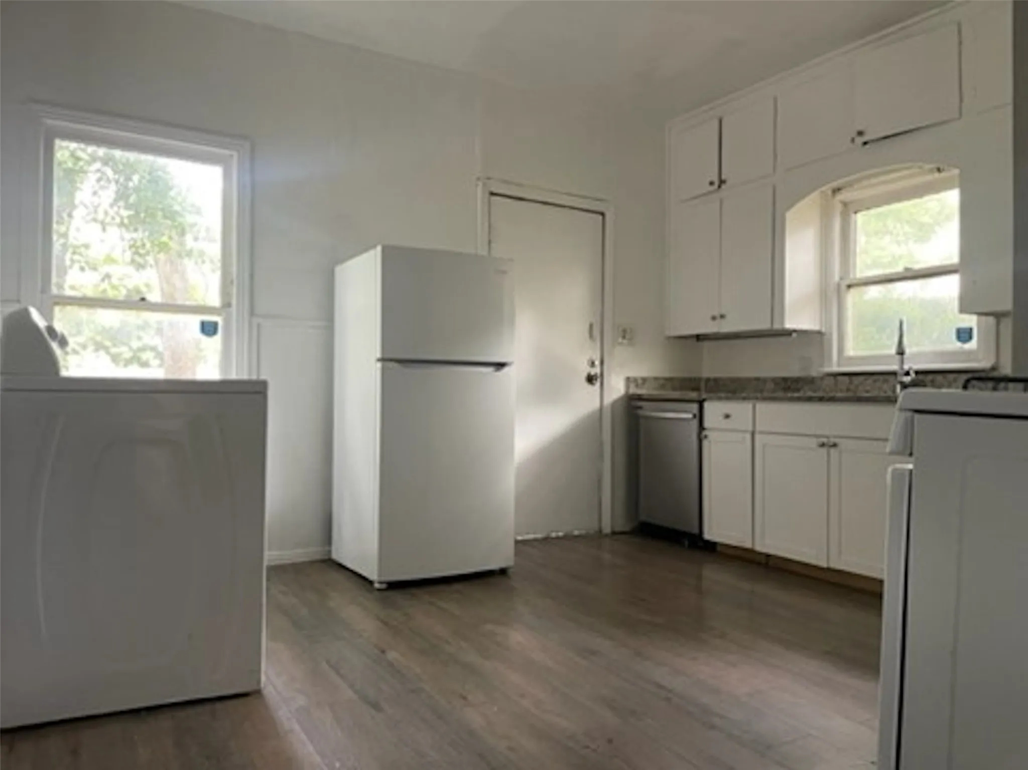 Kitchen featuring white cabinets, freestanding refrigerator, dishwasher, dark countertops, and washer / dryer