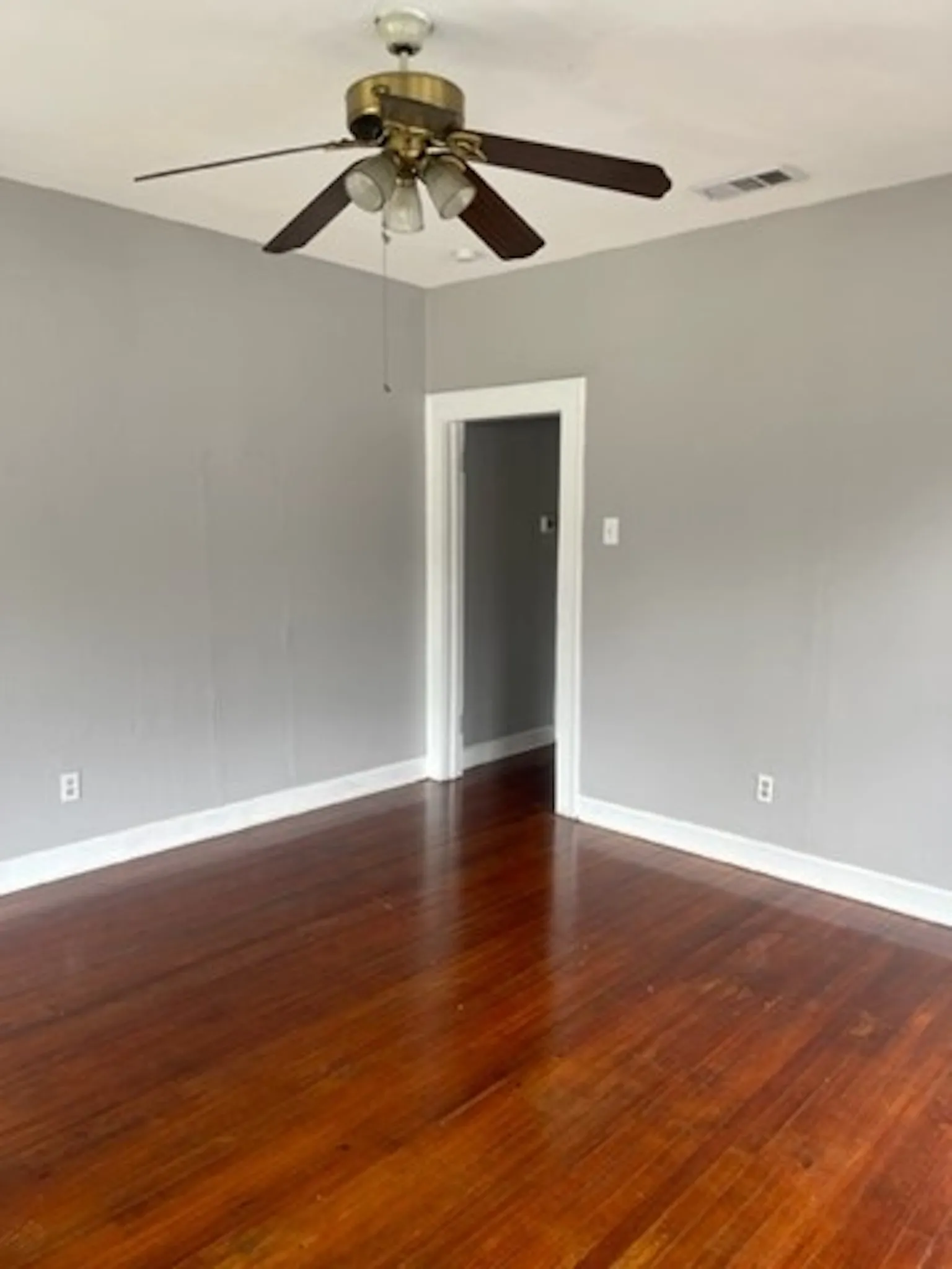 Unfurnished room featuring dark wood-style floors, baseboards, visible vents, and ceiling fan