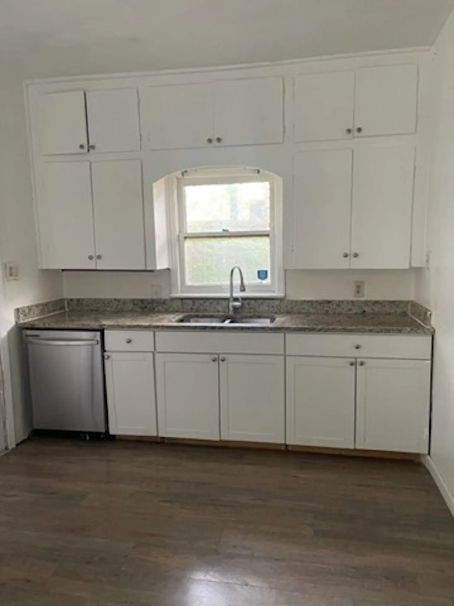 Kitchen featuring dark wood-style floors, dark countertops, white cabinetry, a sink, and dishwasher