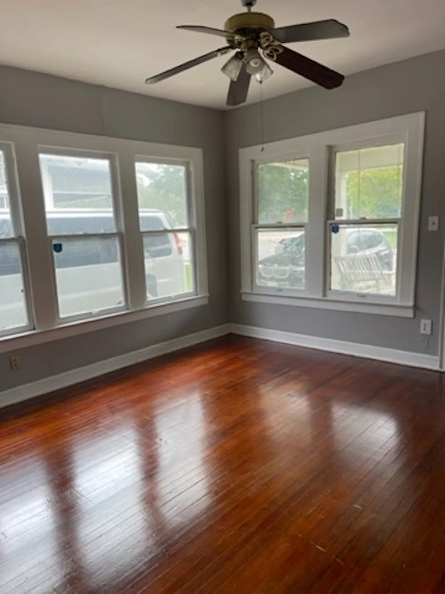 Unfurnished room featuring plenty of natural light, baseboards, ceiling fan, and dark wood-style flooring