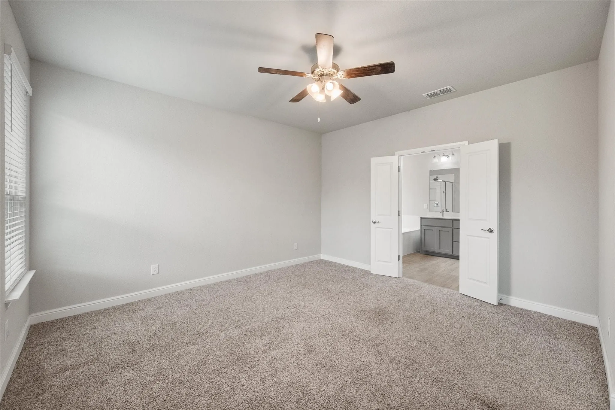 Spacious private bedroom featuring neutral carpeting and a ceiling fan with integrated lighting.