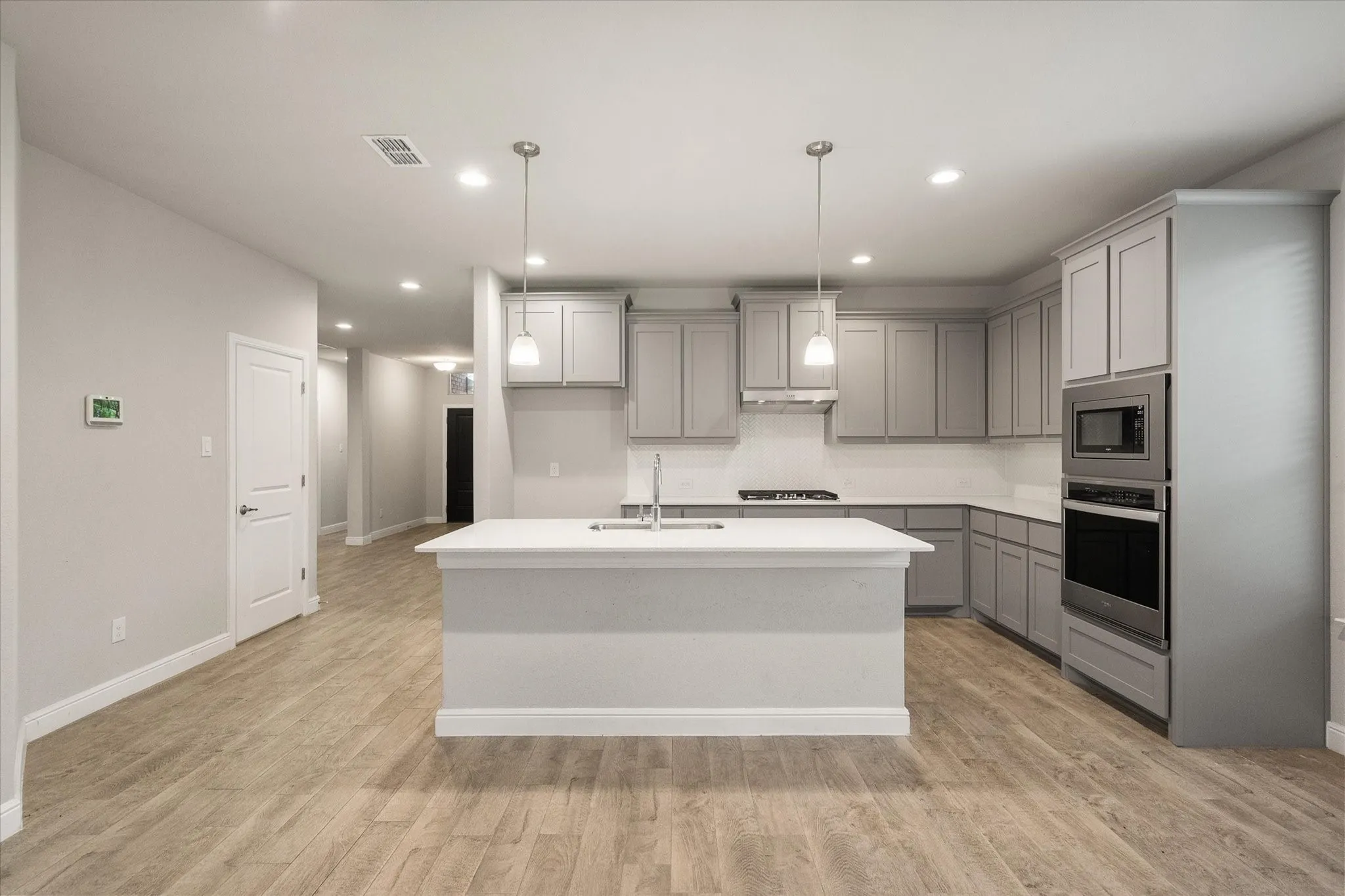 Kitchen featuring an island with double pendant lighting, gray shaker cabinetry, stainless steel appliances, quartz countertops, and wood-look tile flooring