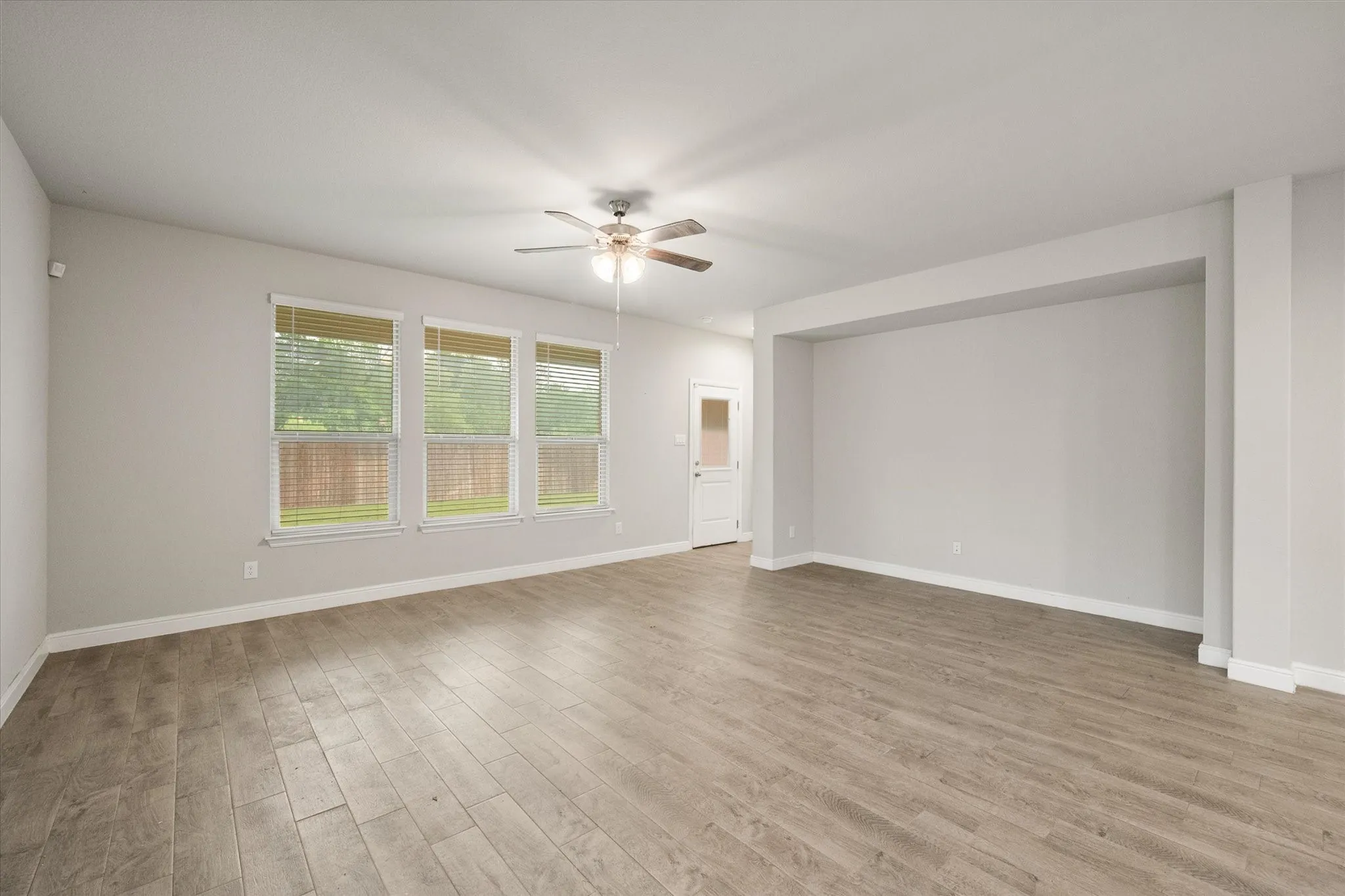 Spacious room featuring wood-look tile flooring, three windows with blinds, a ceiling fan, and a recessed wall section perfect for a large tv!
