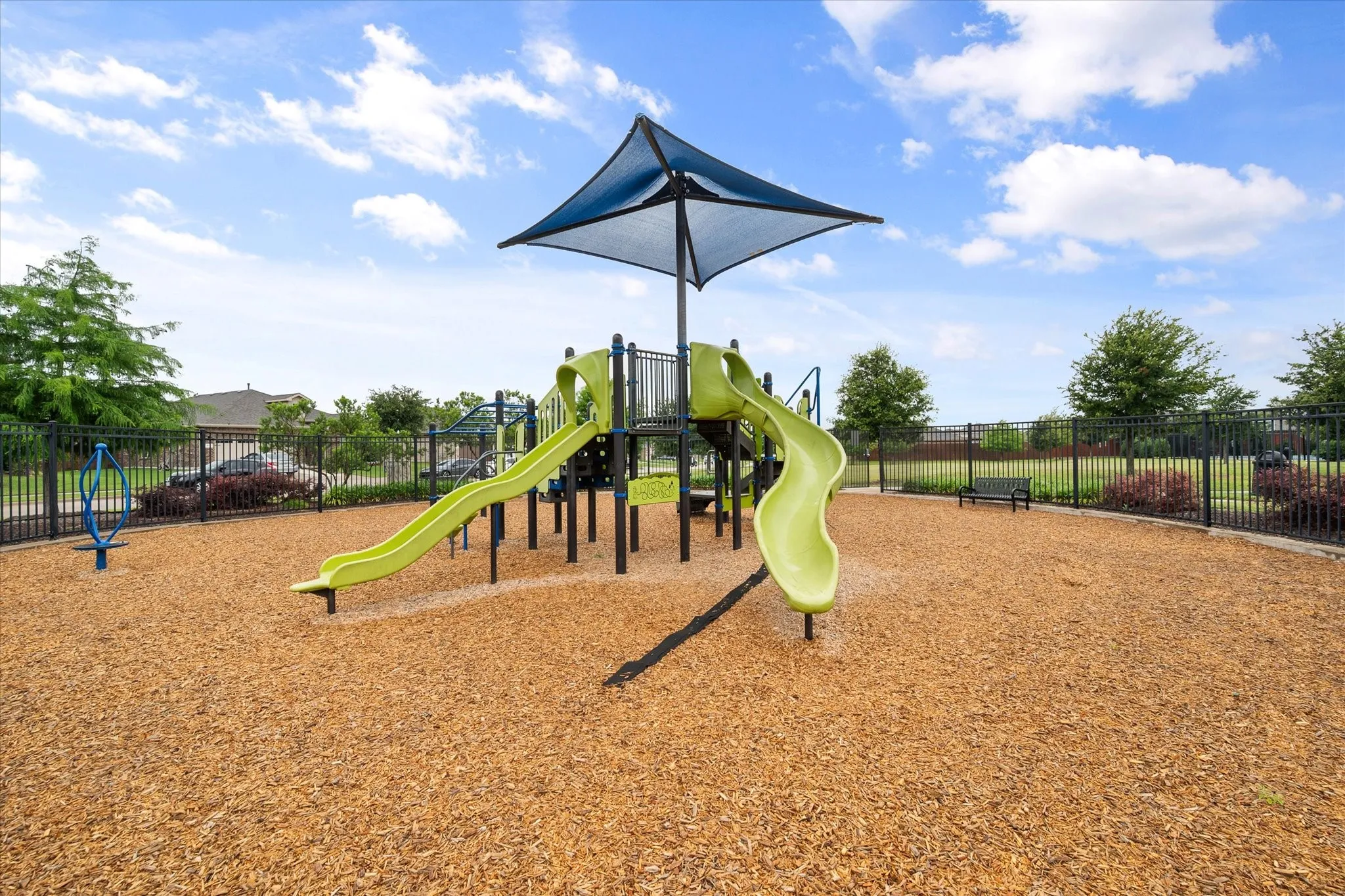 Playground area featuring a multi-level play structure, dual slides, a protective shade canopy, and wood chip surfacing