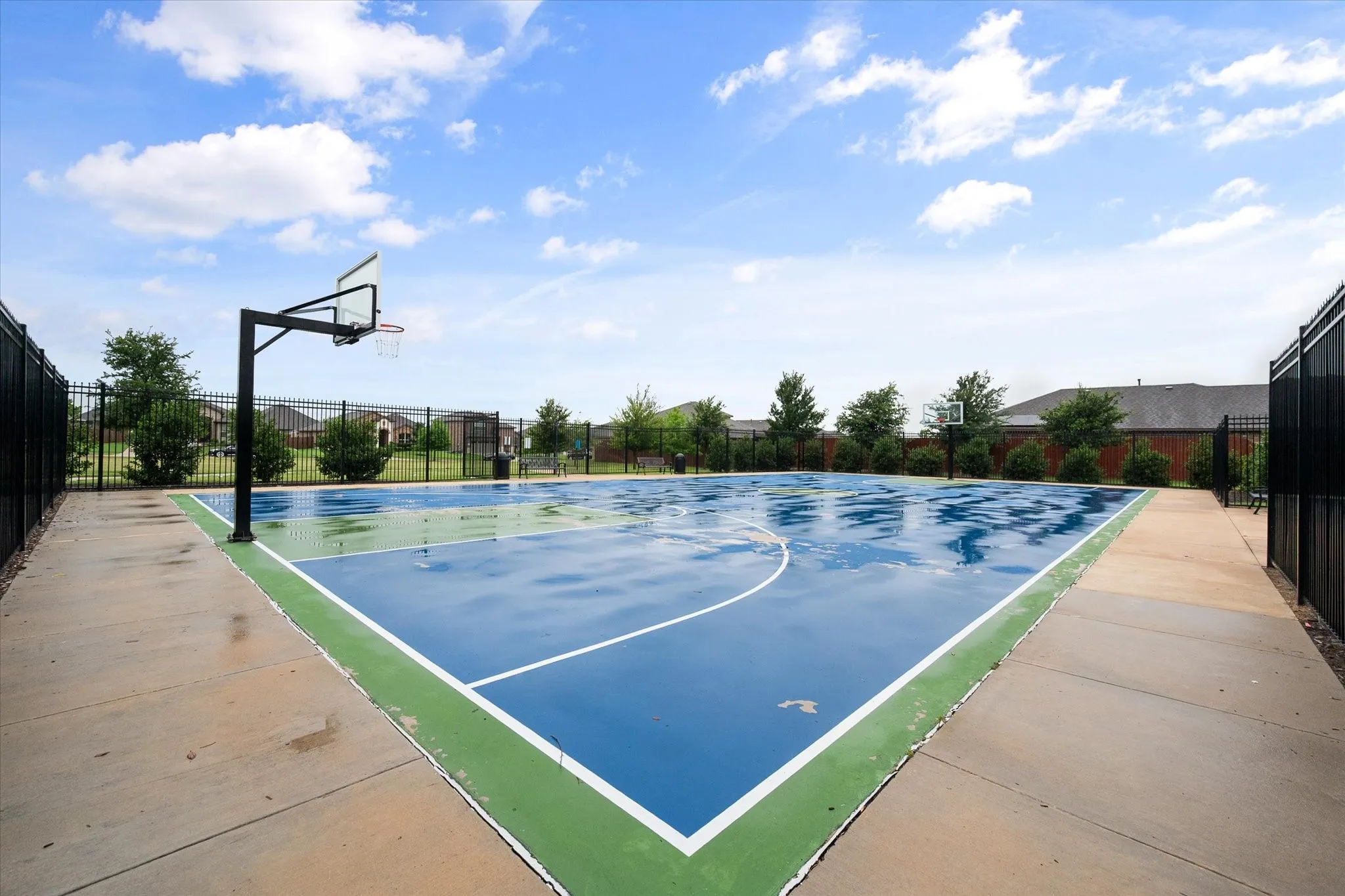 Multi-sport court featuring a blue and green playing surface, perimeter fencing, and concrete pathways